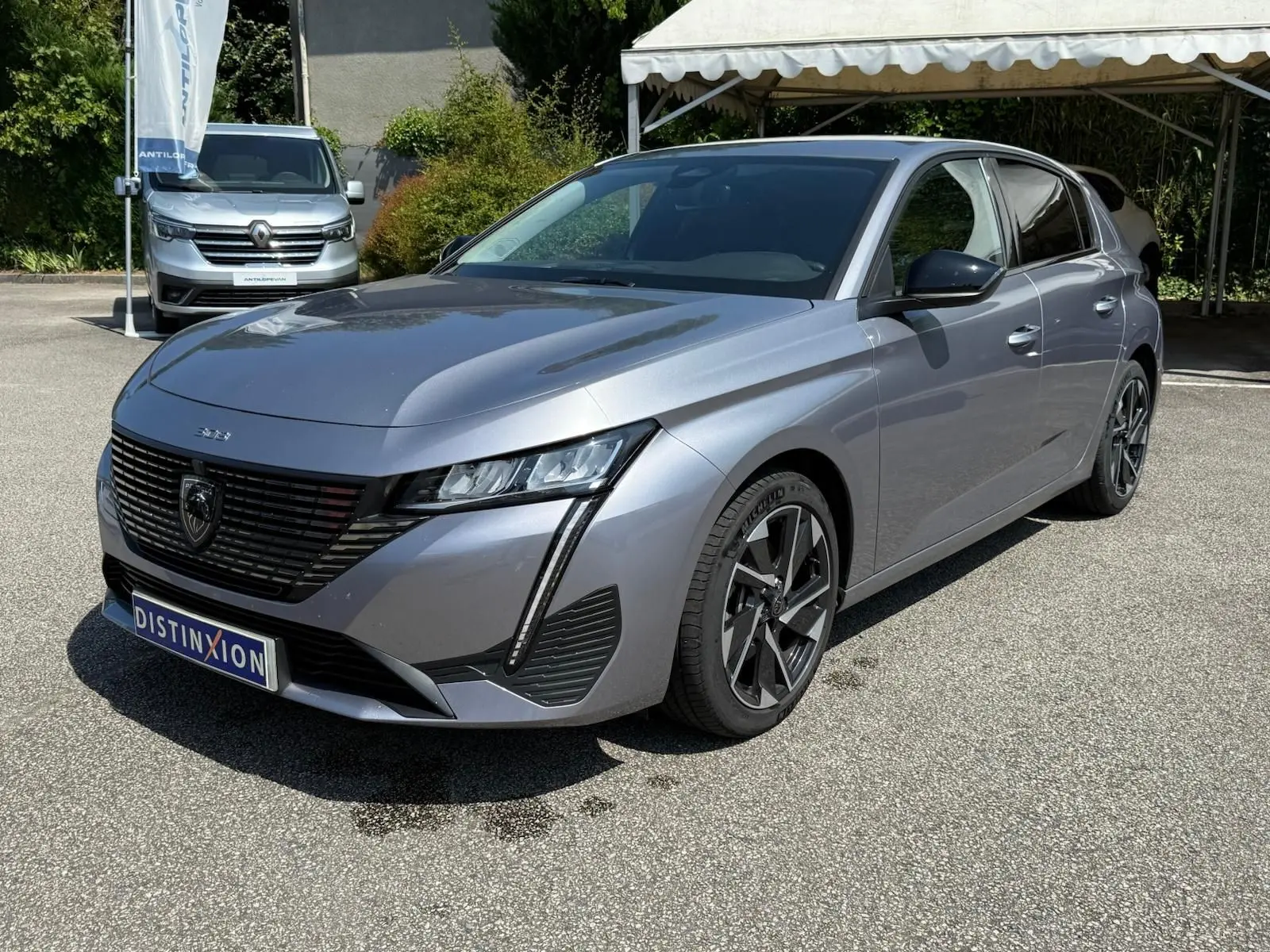 Peugeot 308 gris Artense vue 3/4 avant droit, mettant en valeur sa calandre noire et ses phares LED fins.