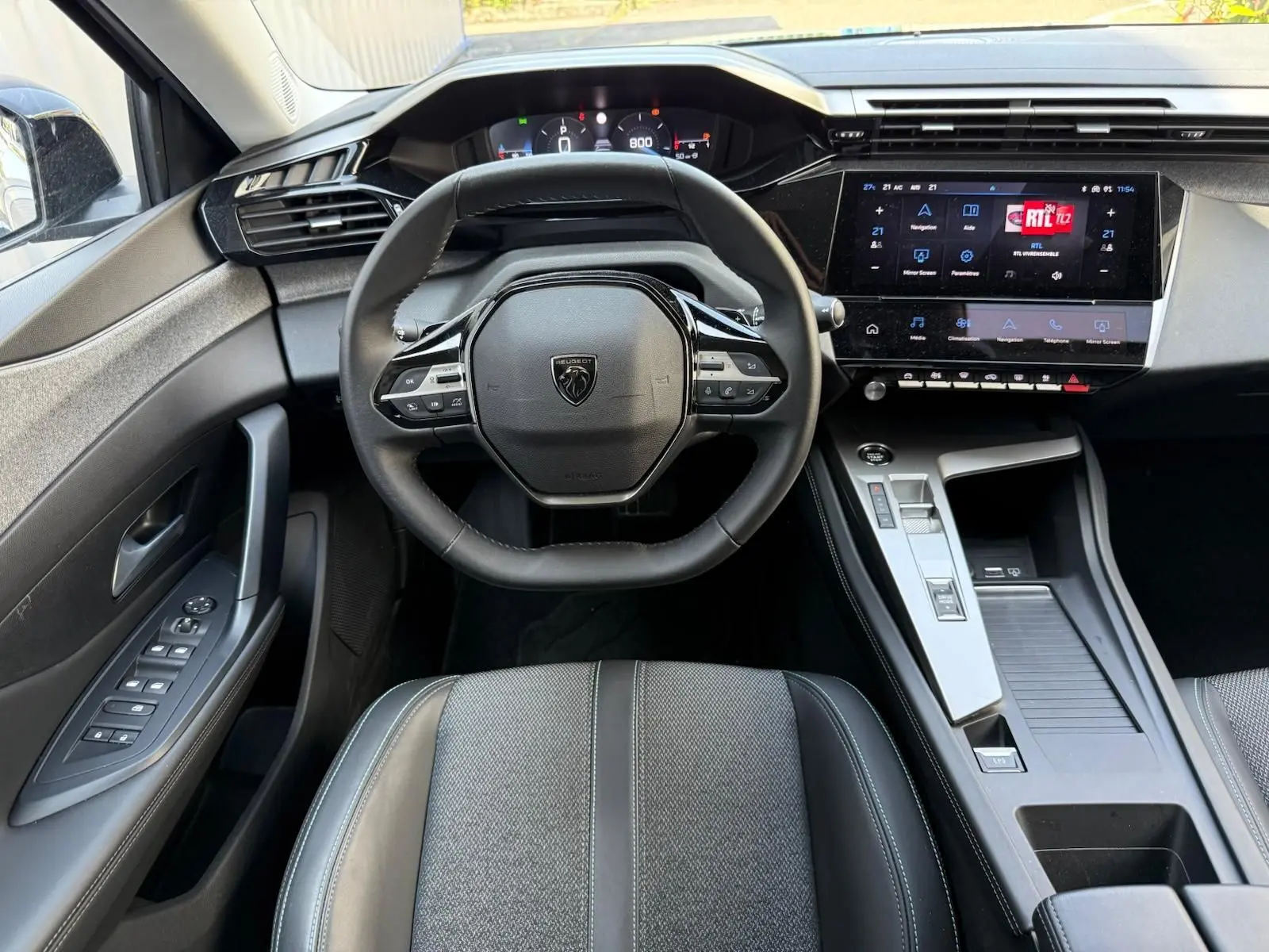 Vue intérieure centrée sur le volant et la console centrale d'une Peugeot 308 2024 avec écran tactile et finitions modernes.