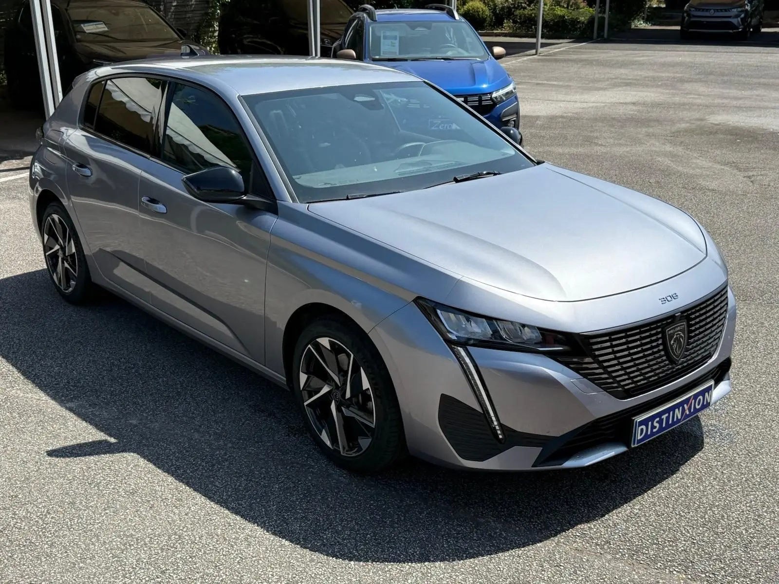 Vue 3/4 avant gauche d'une Peugeot 308 gris Artense 2024 avec calandre noire et phares LED distinctifs.