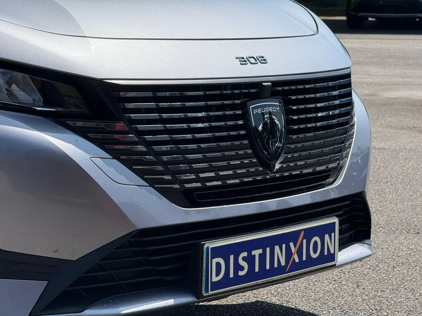 Vue rapprochée avant d'une Peugeot 308 gris Artense avec calandre noire et logo lion central bien visible.