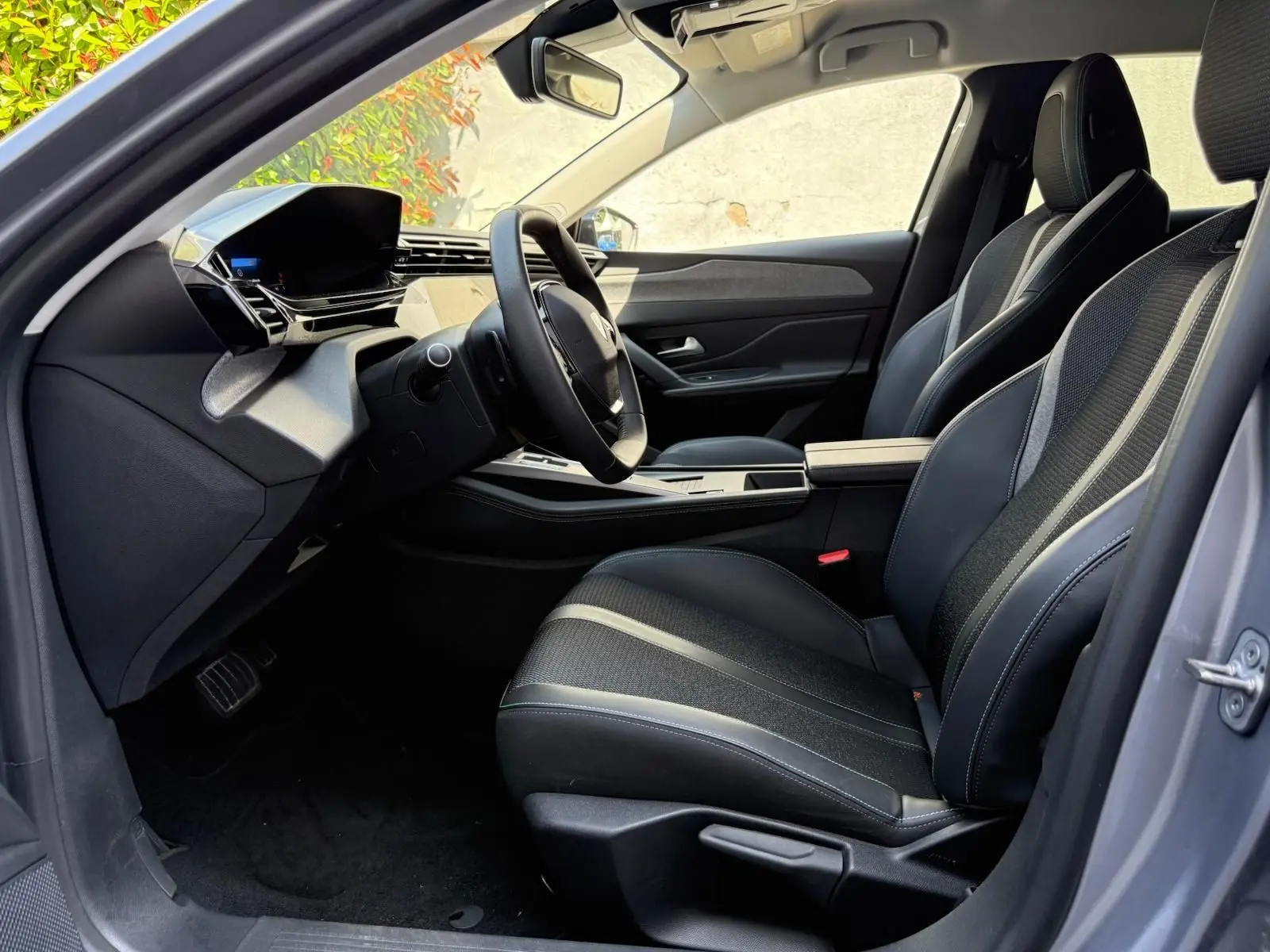 Vue intérieure côté conducteur de la Peugeot 308 2024 gris Artense, avec sièges noirs et tableau de bord moderne.