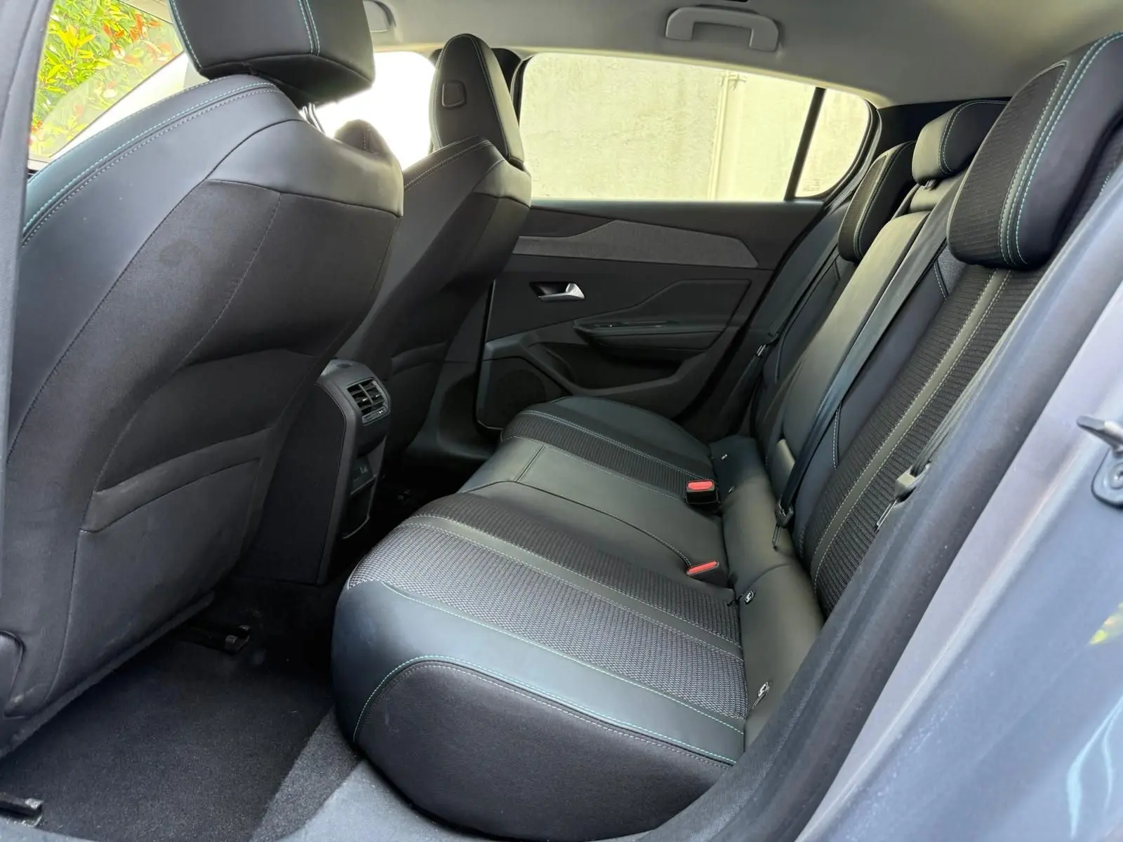 Vue intérieure côté droit des sièges arrière en cuir noir avec surpiqûres vertes d'une Peugeot 308 gris Artense 2024.