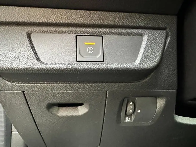 Gros plan sur le bouton de verrouillage central et réglage des phares dans l'habitacle noir du Dacia Jogger 2025.