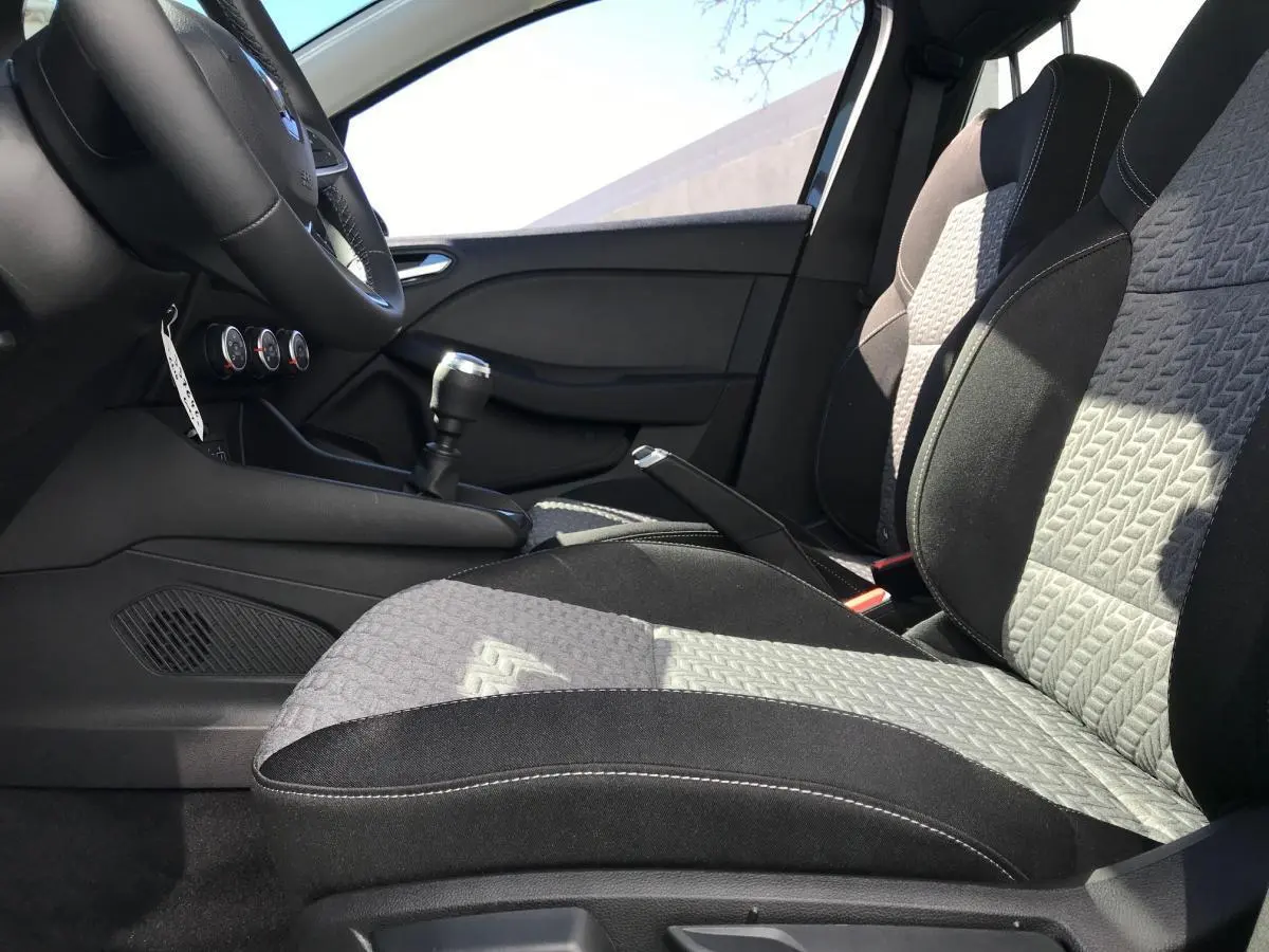 Intérieur avant de la Renault Clio 2021, vue côté gauche sur les sièges tissu noir et gris avec surpiqûres blanches et levier de vitesse manuel.