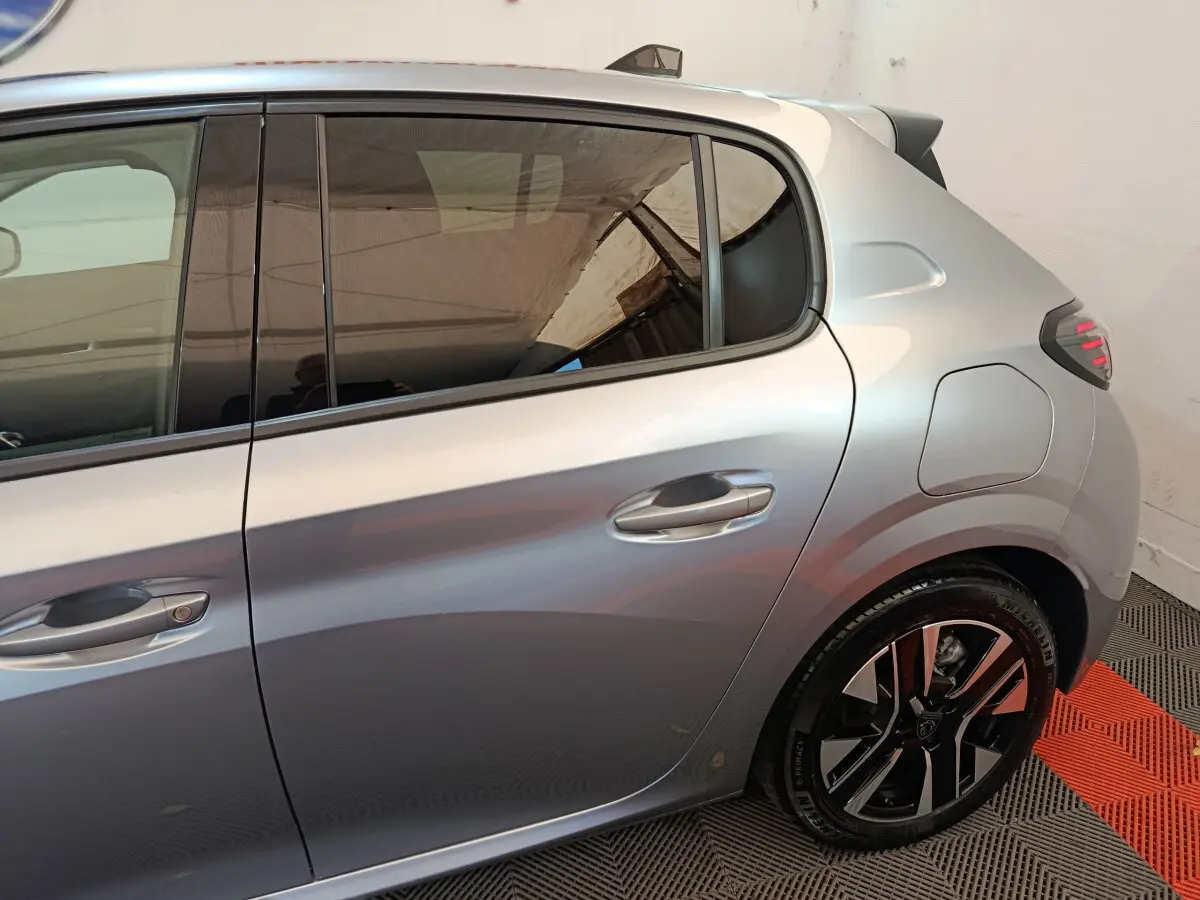 Vue latérale droite sur la partie arrière d'une Peugeot 208 gris clair avec jante alliage et porte-fuel visible.