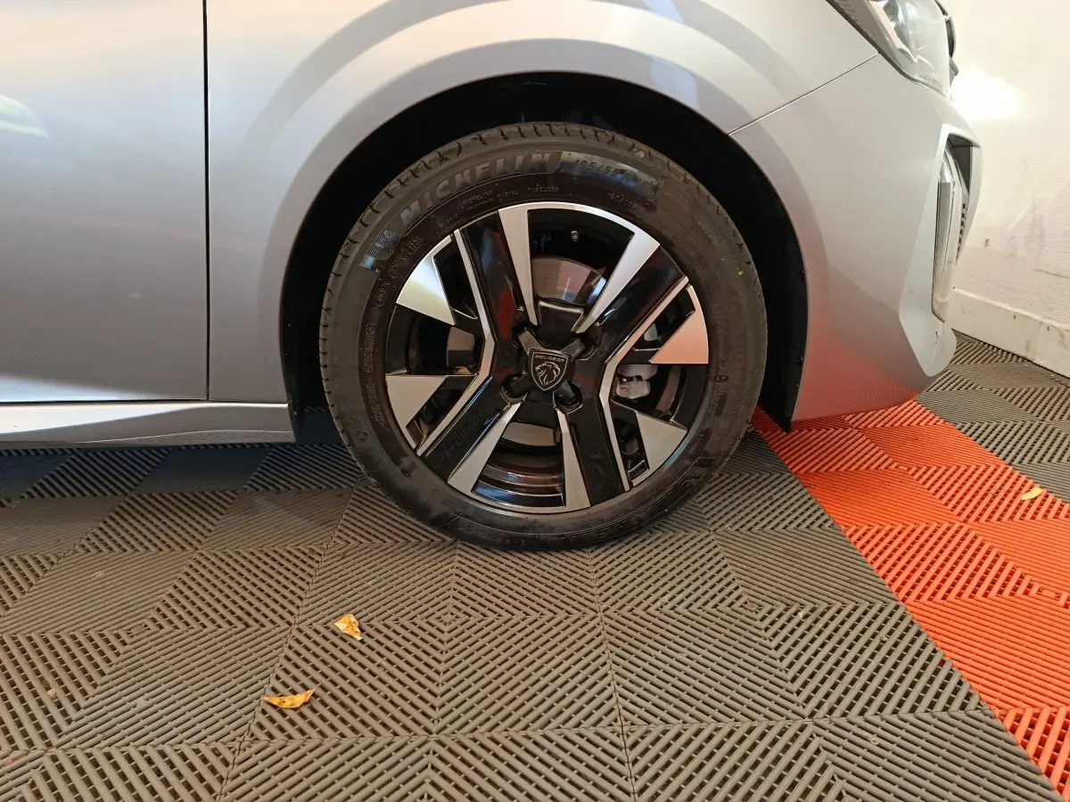 Gros plan sur la roue avant droite d'une Peugeot 208 gris clair, avec jante alliage noire et argentée au design moderne.