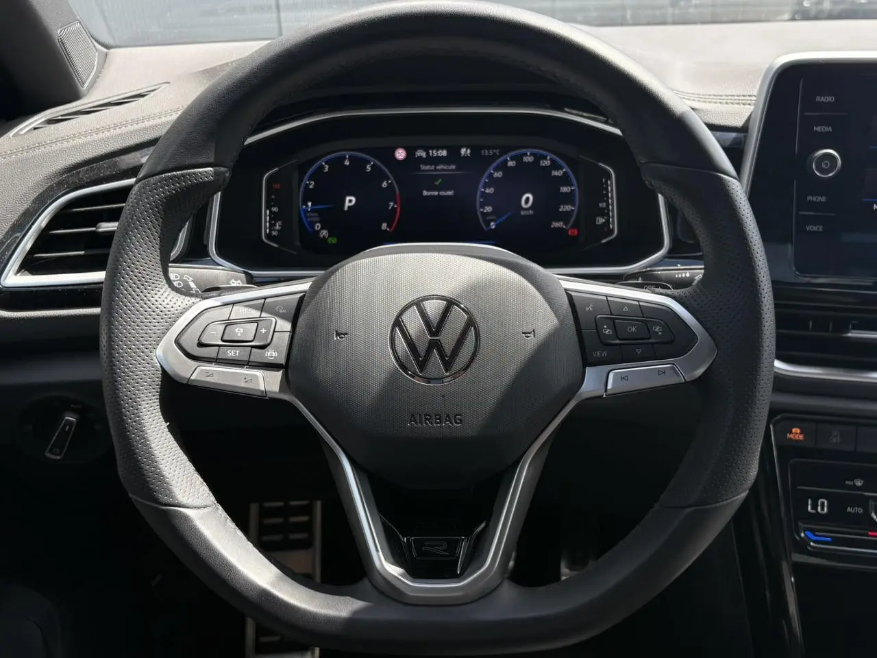 Vue rapprochée du volant sport multifonction R-Line noir du Volkswagen T-Roc 2025 avec tableau de bord digital en arrière-plan.