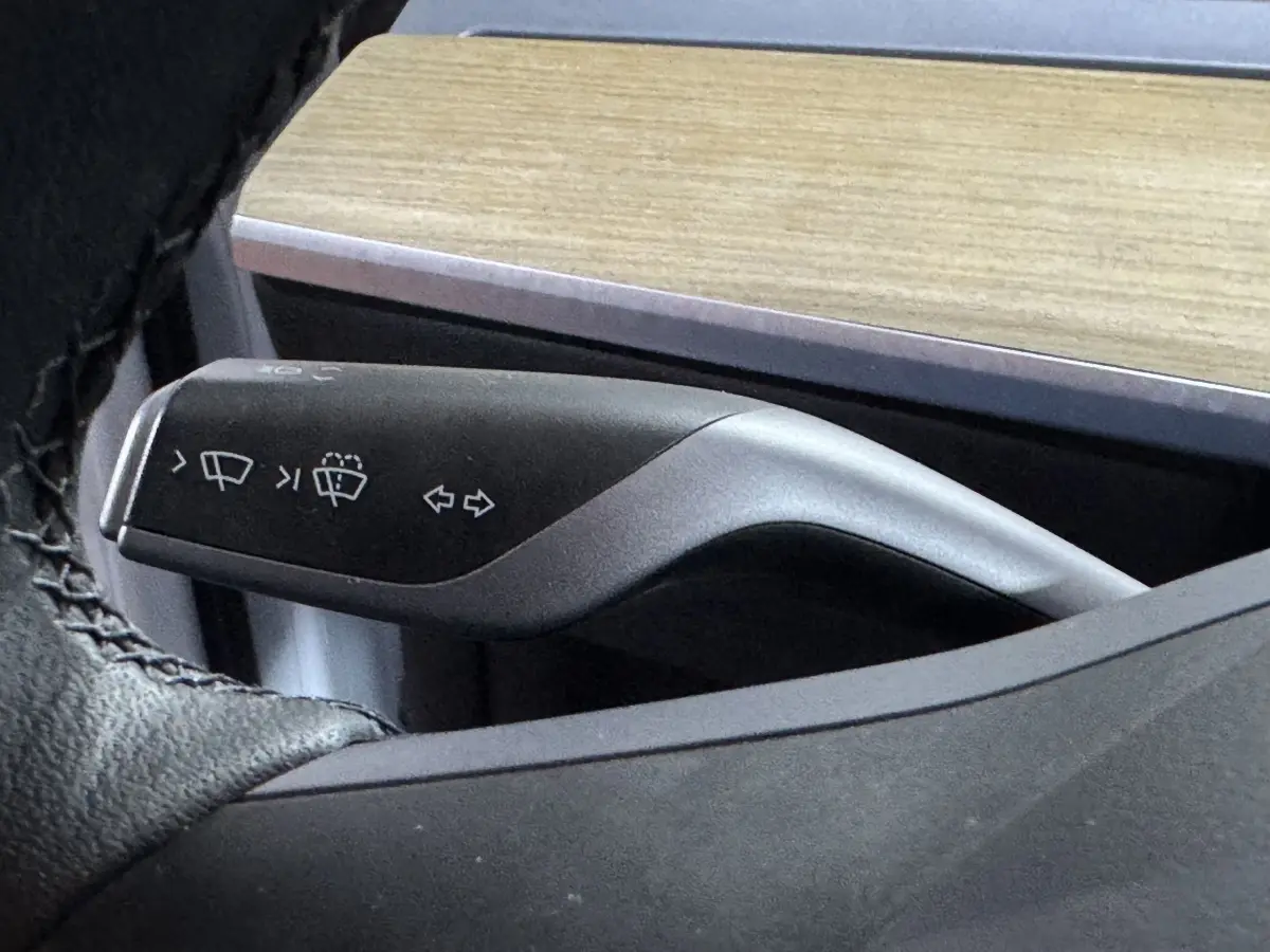 Gros plan sur la commande de clignotants et essuie-glaces du Tesla Model Y blanc, intérieur avec tableau de bord bois.