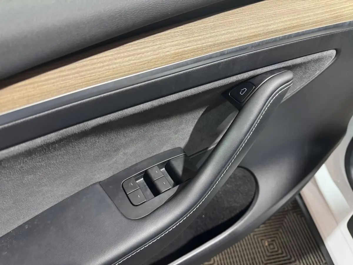 Gros plan sur la garniture intérieure côté conducteur de la Tesla Model Y blanche, avec insert bois et commandes de fenêtres.