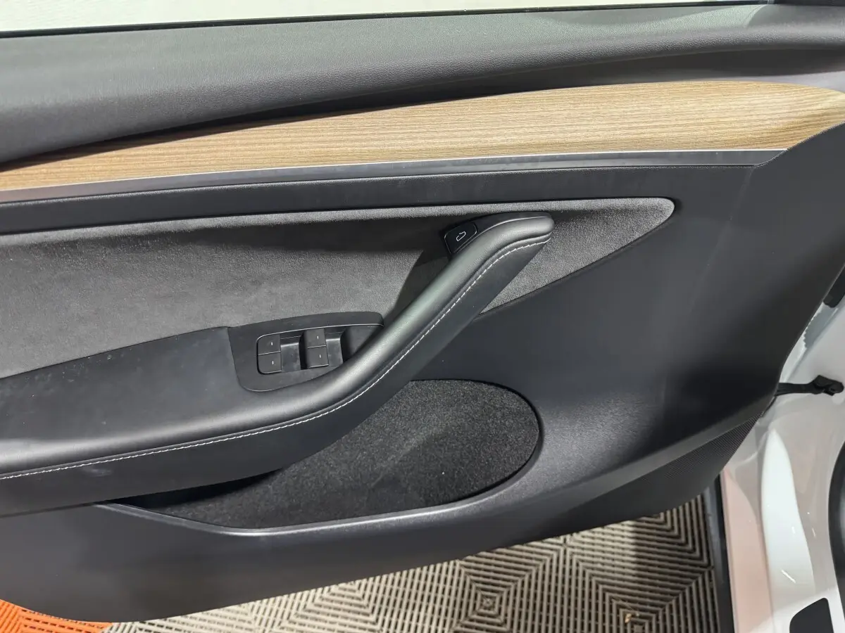 Gros plan sur la porte avant gauche blanche d'une Tesla Model Y, avec garniture noire et insert bois clair.