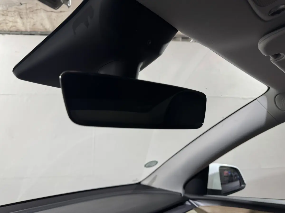 Rétroviseur intérieur noir avec vue partielle du tableau de bord et du montant côté droit d'une Tesla Model Y blanche.