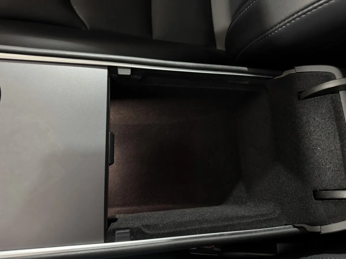 Vue rapprochée de la console centrale ouverte du Tesla Model Y blanc, montrant un compartiment de rangement noir.