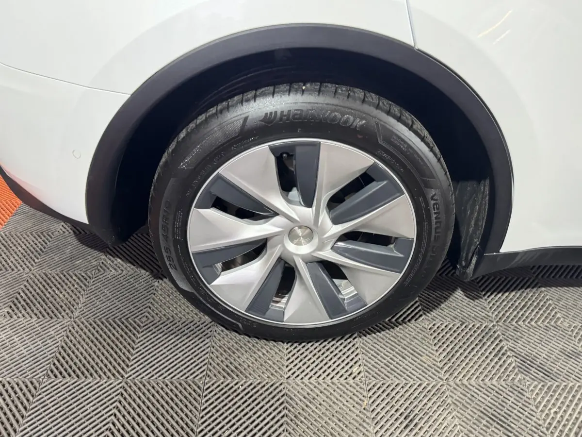 Gros plan sur la roue arrière droite d'une Tesla Model Y blanche, mettant en valeur la jante moderne et le pneu Hankook.