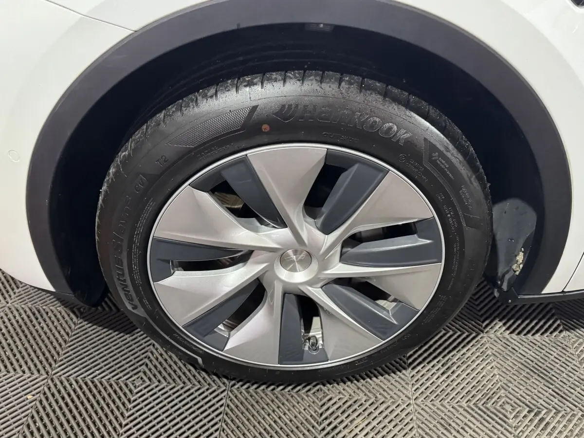 Gros plan sur la roue avant droite d'une Tesla Model Y blanche, avec jante aérodynamique grise et noire.