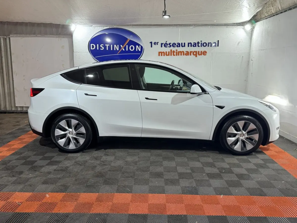 Tesla Model Y blanc en vue profil côté gauche, stationné en intérieur avec logo Distinxion en arrière-plan.
