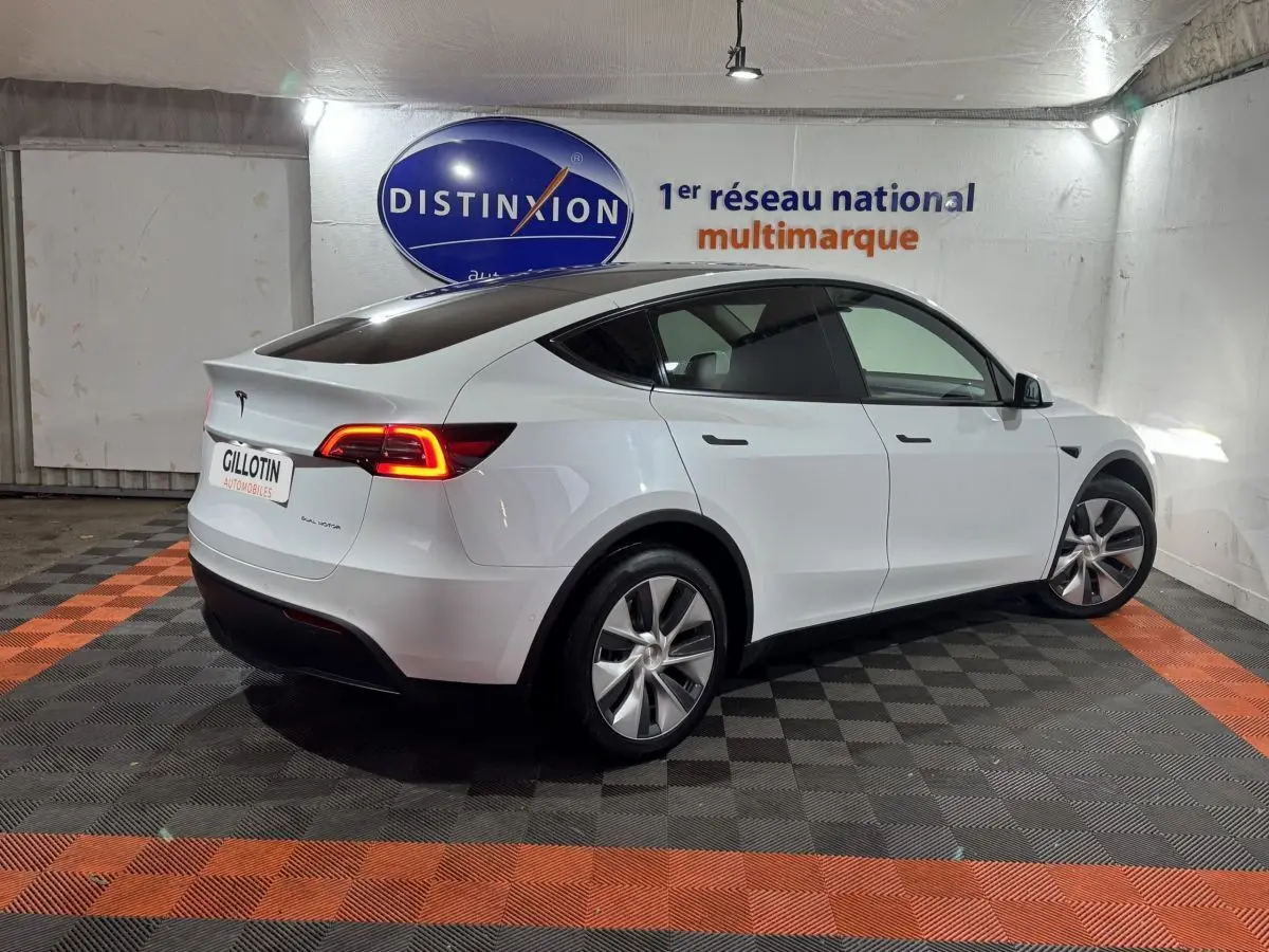 Tesla Model Y blanc en 3/4 arrière droit dans un showroom avec feux arrière LED allumés.