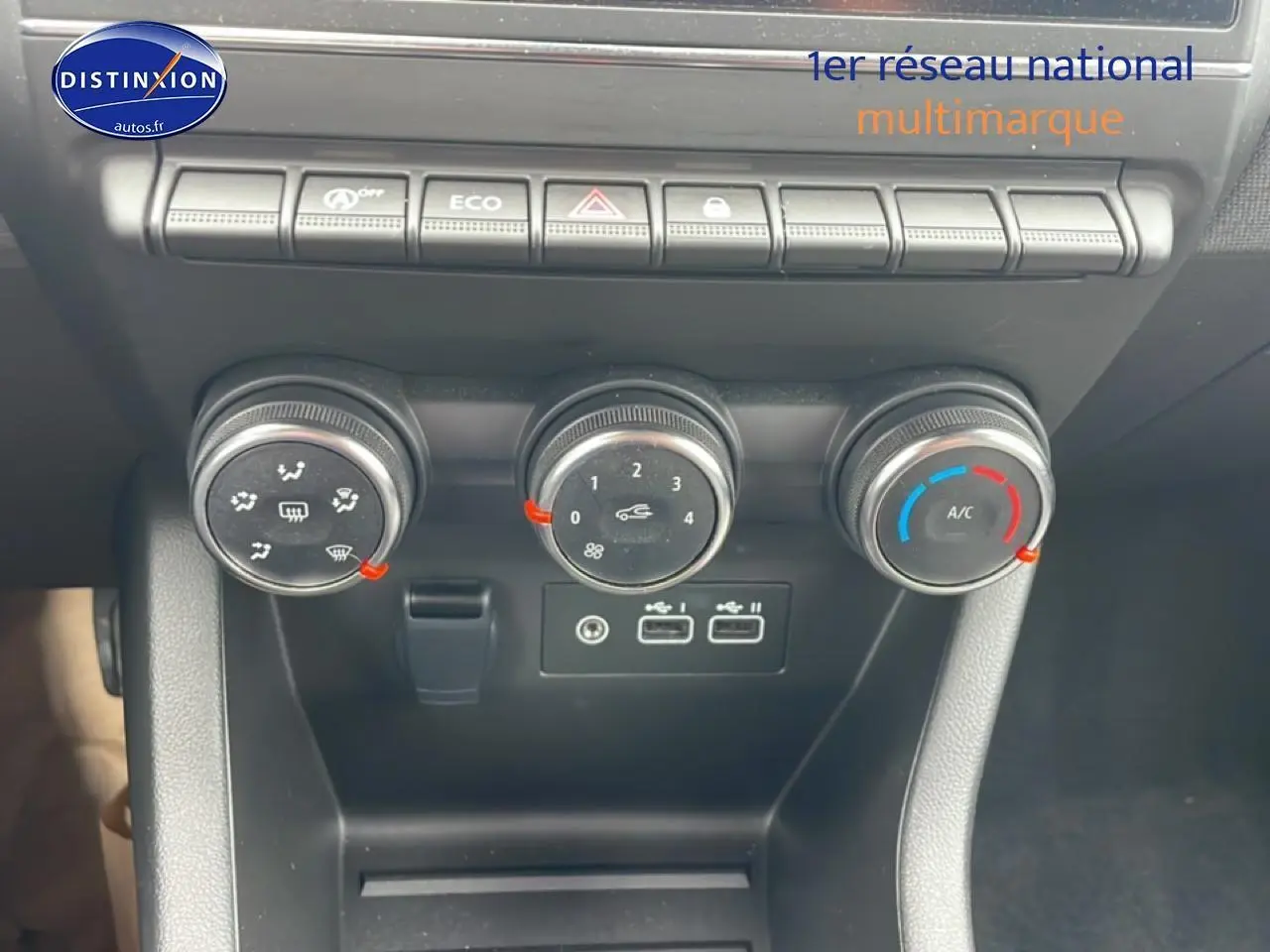Vue rapprochée des commandes de climatisation et des ports USB d'une Renault Clio V blanche, tableau de bord noir.