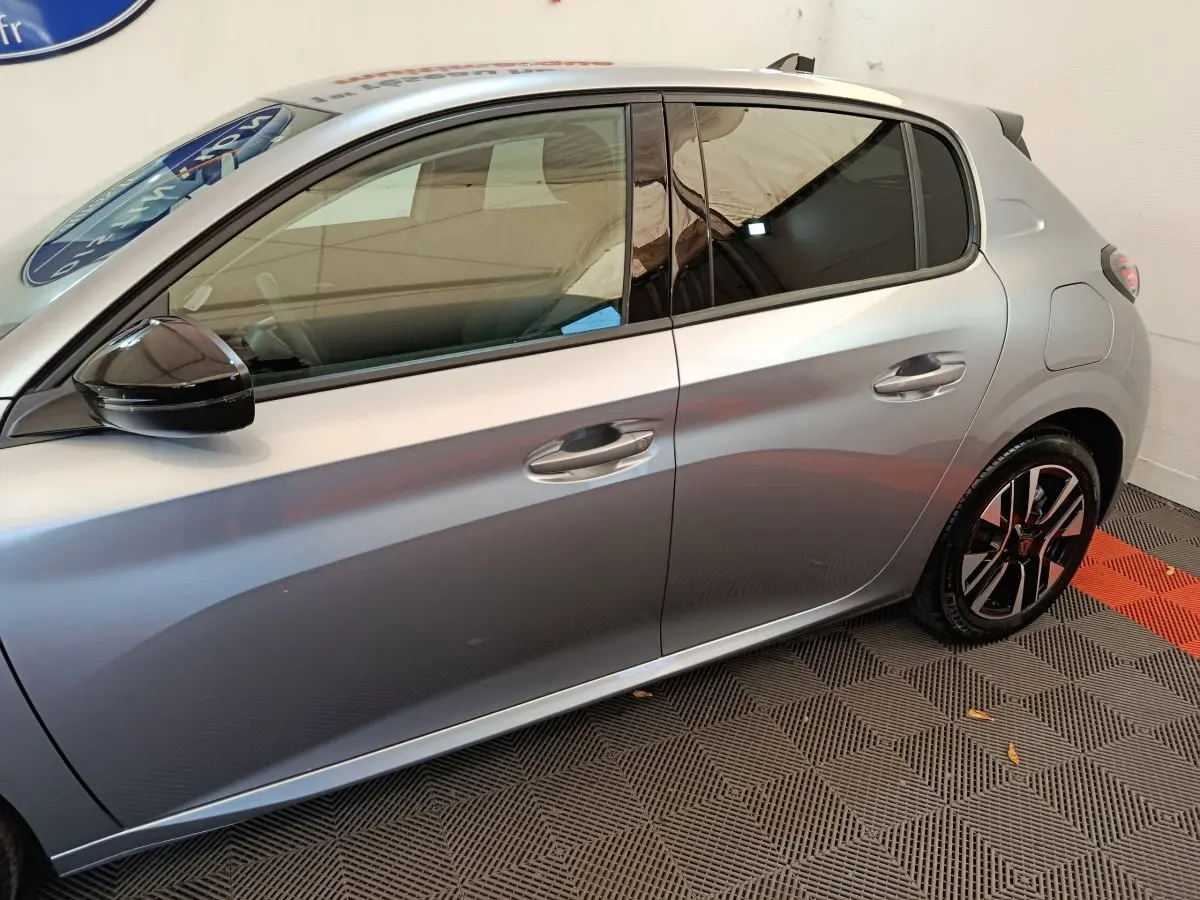 Profil droit d'une Peugeot 208 gris clair 2025 avec rétroviseurs noirs et jantes alliage bicolores.