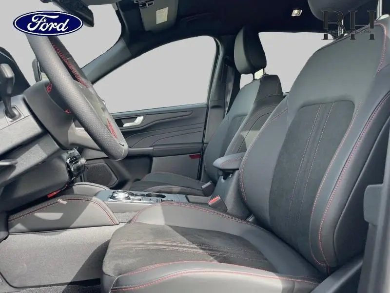 Vue intérieure côté conducteur du Ford Kuga 2026 avec sièges sport en suédine noire et surpiqûres rouges.