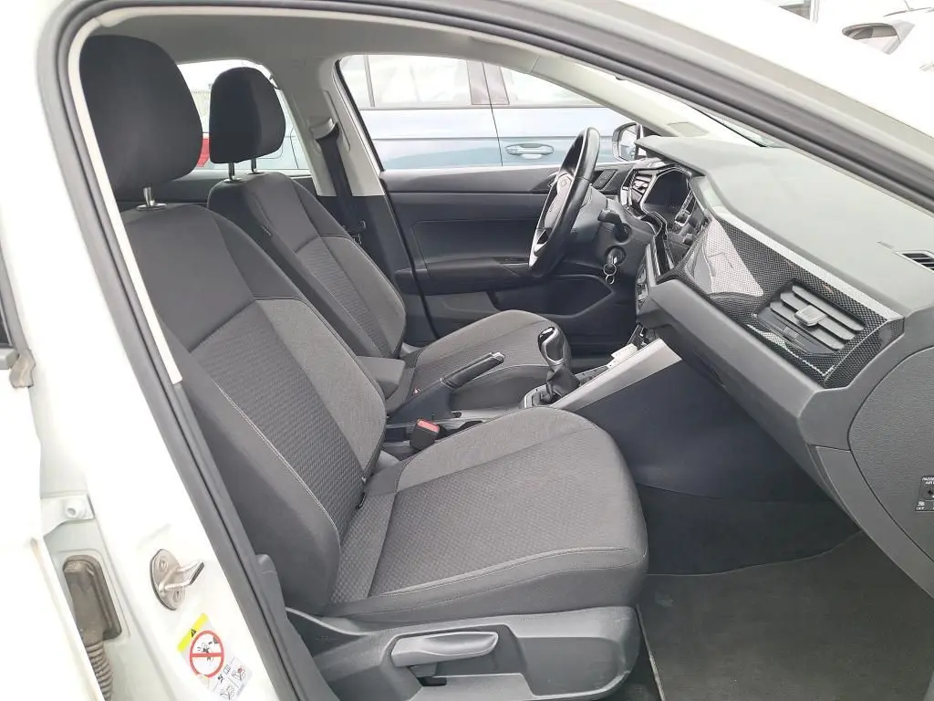 Vue intérieure côté conducteur de la Volkswagen Polo blanche 2023, sièges tissu gris et tableau de bord moderne.
