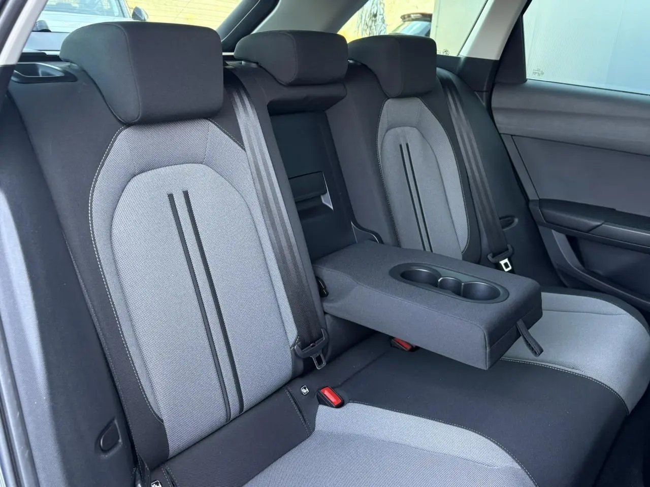 Vue intérieure des sièges arrière gris clair et noir du SEAT LEON ST avec accoudoir central et porte-gobelets déployé.