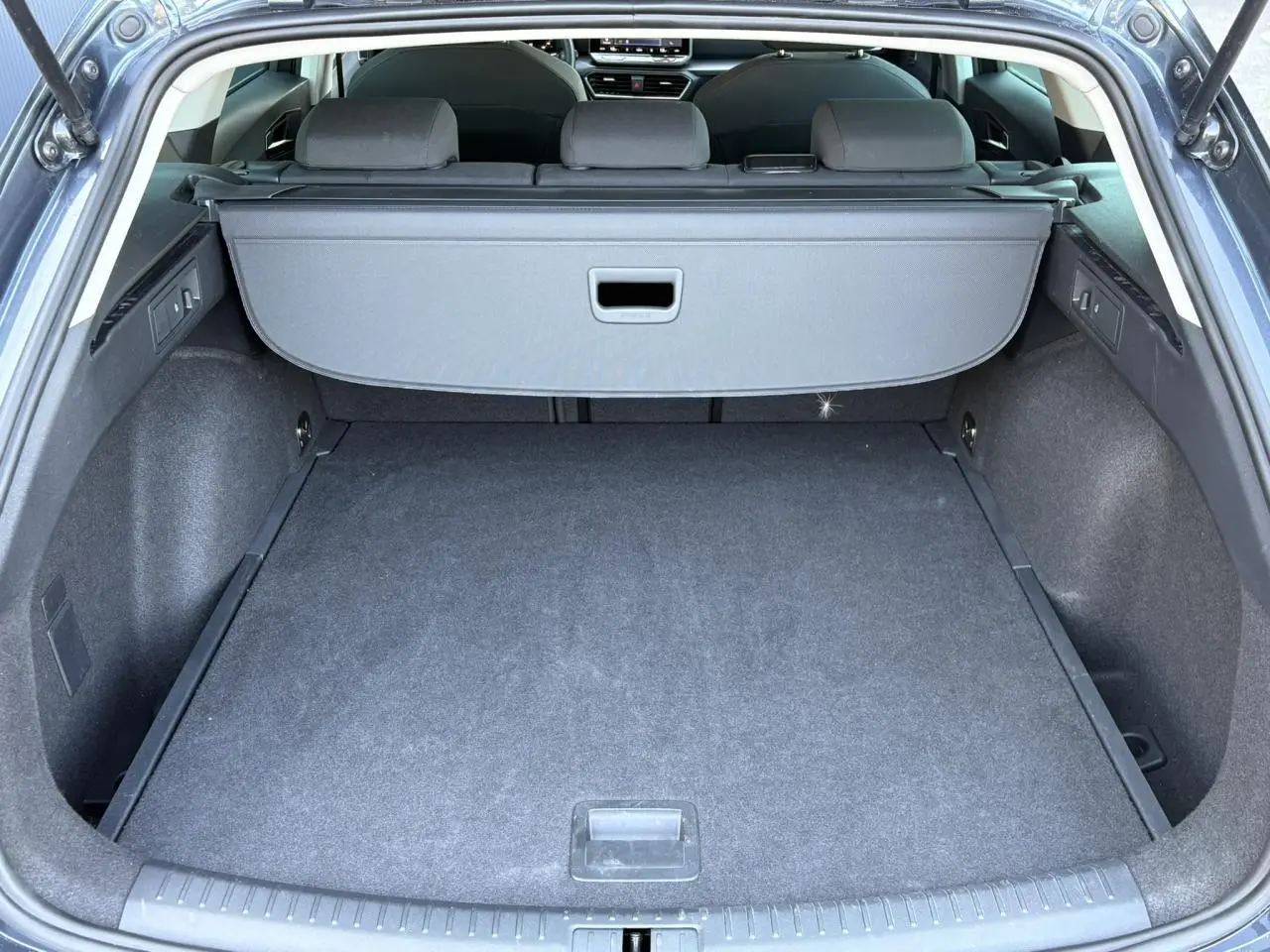 Coffre ouvert vu de l'arrière d'une SEAT LEON ST gris magnétique avec cache-bagages et sièges arrière rabattus.