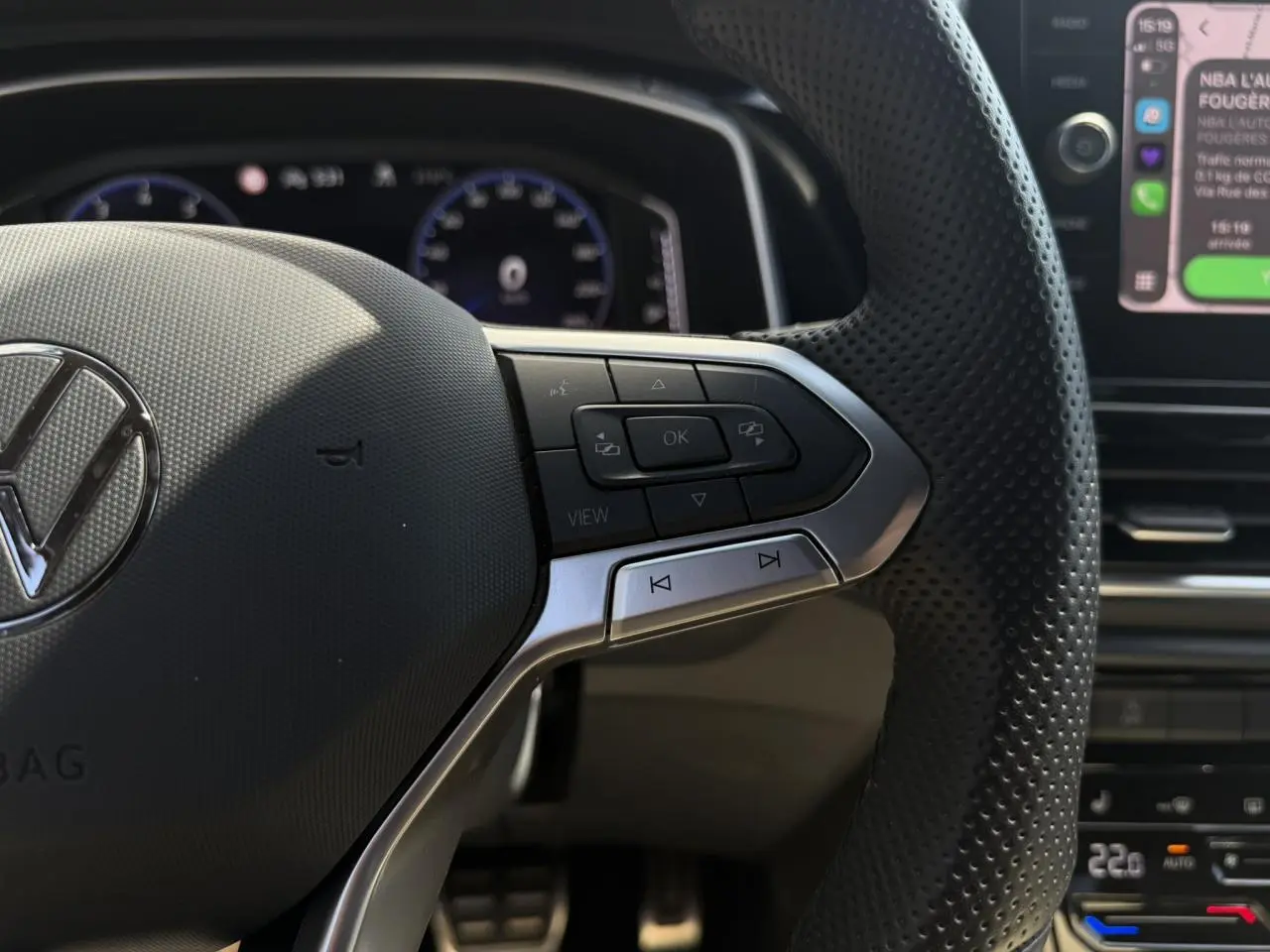 Gros plan sur le volant multifonction en cuir perforé du Volkswagen T-Roc 2025 avec commandes intégrées et tableau de bord digital en arrière-plan.