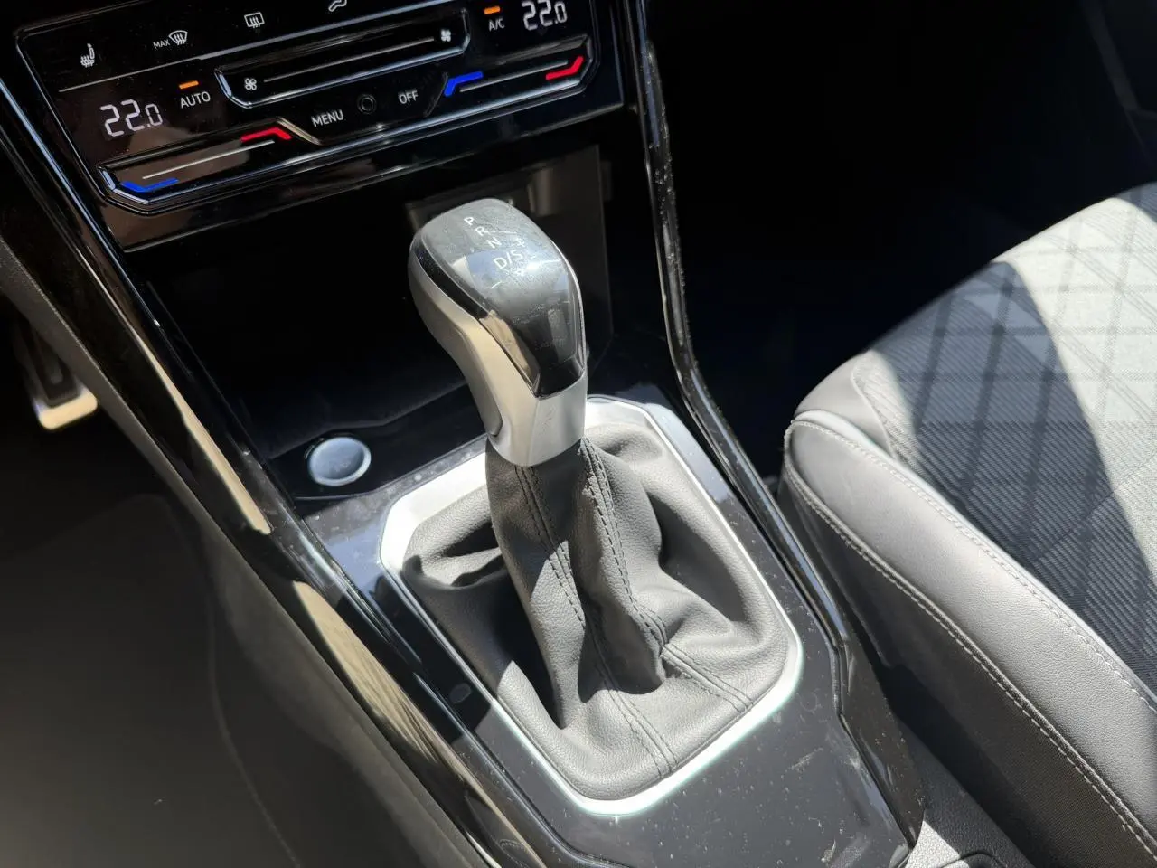 Gros plan sur la commande de boîte automatique et la console centrale noire du Volkswagen T-Roc 2025, siège gris partiellement visible.