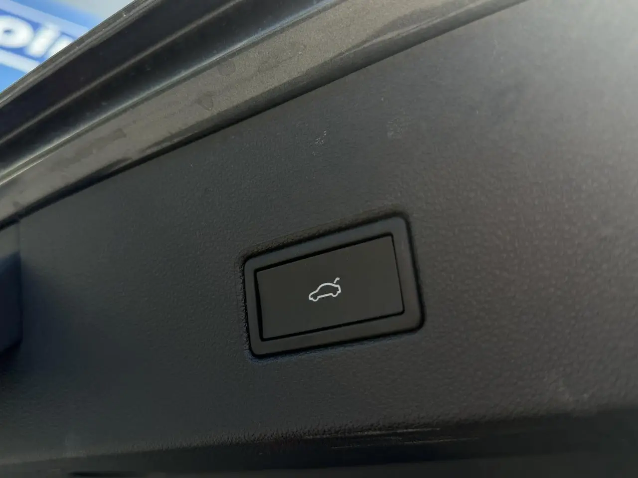 Bouton noir d'ouverture du hayon électrique sur le coffre d'un Volkswagen T-Roc gris Indium, vue rapprochée intérieure.