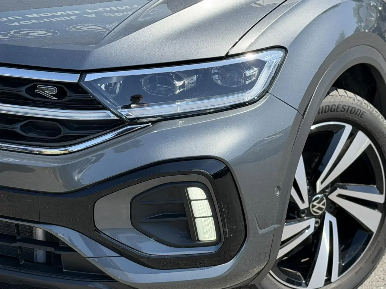 Gros plan sur l'avant droit du Volkswagen T-Roc gris Indium, mettant en valeur le projecteur Matrix LED et la jante Nevada 18 pouces.