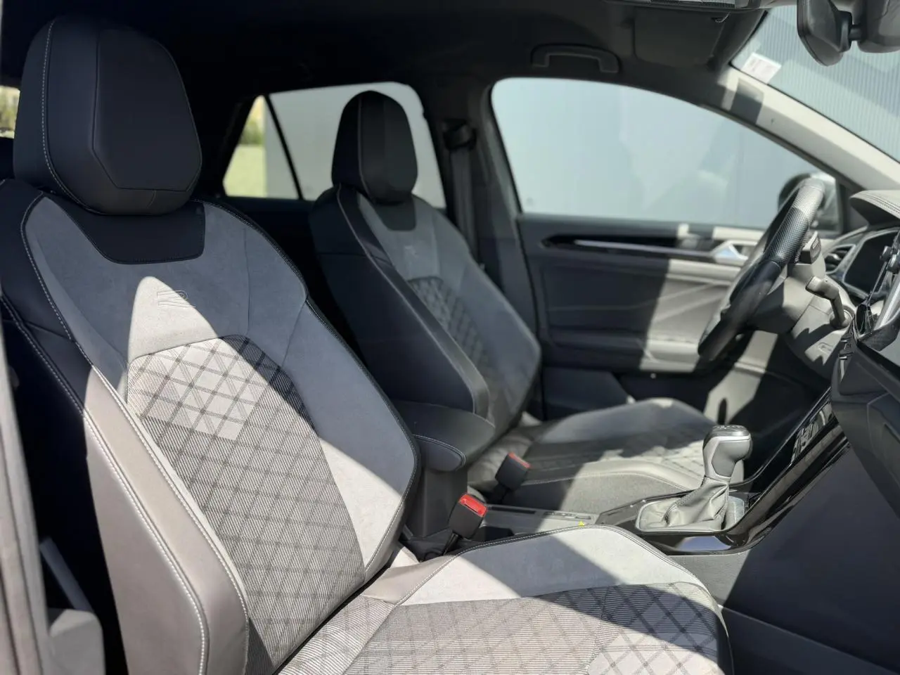 Vue intérieure côté gauche montrant les sièges avant gris avec surpiqûres et logo R-Line du Volkswagen T-Roc 2025.