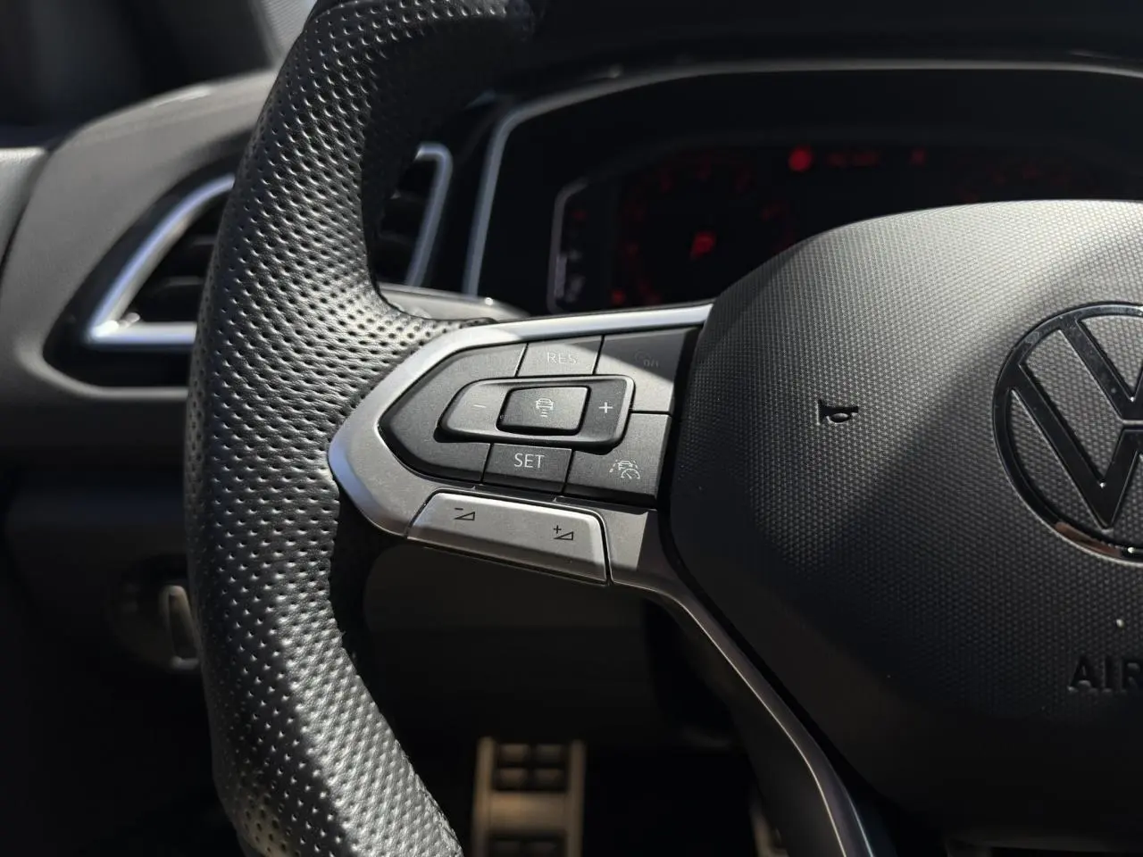 Gros plan sur le volant perforé noir du Volkswagen T-Roc 2025 avec commandes multifonctions côté gauche et logo VW central.
