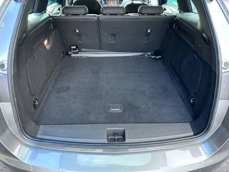 Coffre ouvert vu de l'arrière de l'Opel Astra Sports Tourer gris cosmique avec banquette arrière rabattable et tapis noir.
