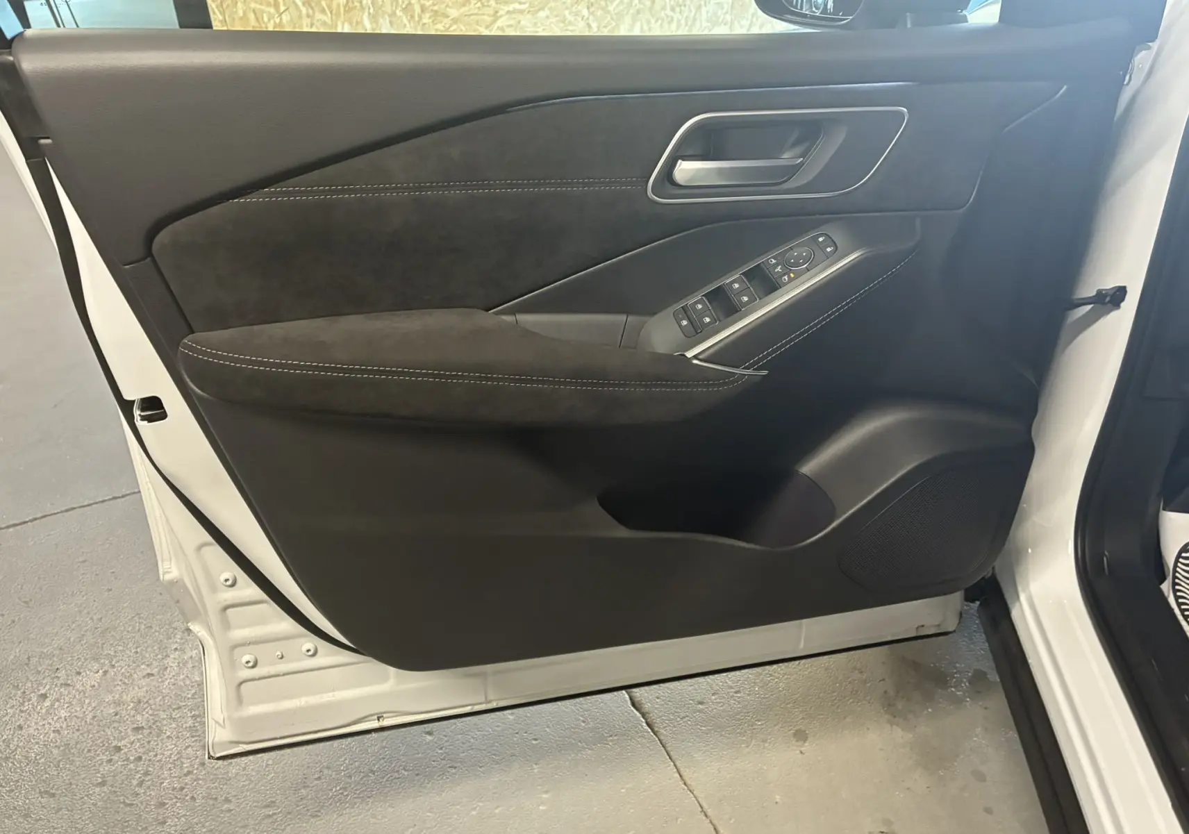 Vue intérieure côté gauche de la porte avant d'un Nissan Qashqai blanc nacré avec garniture noire et commandes électriques.