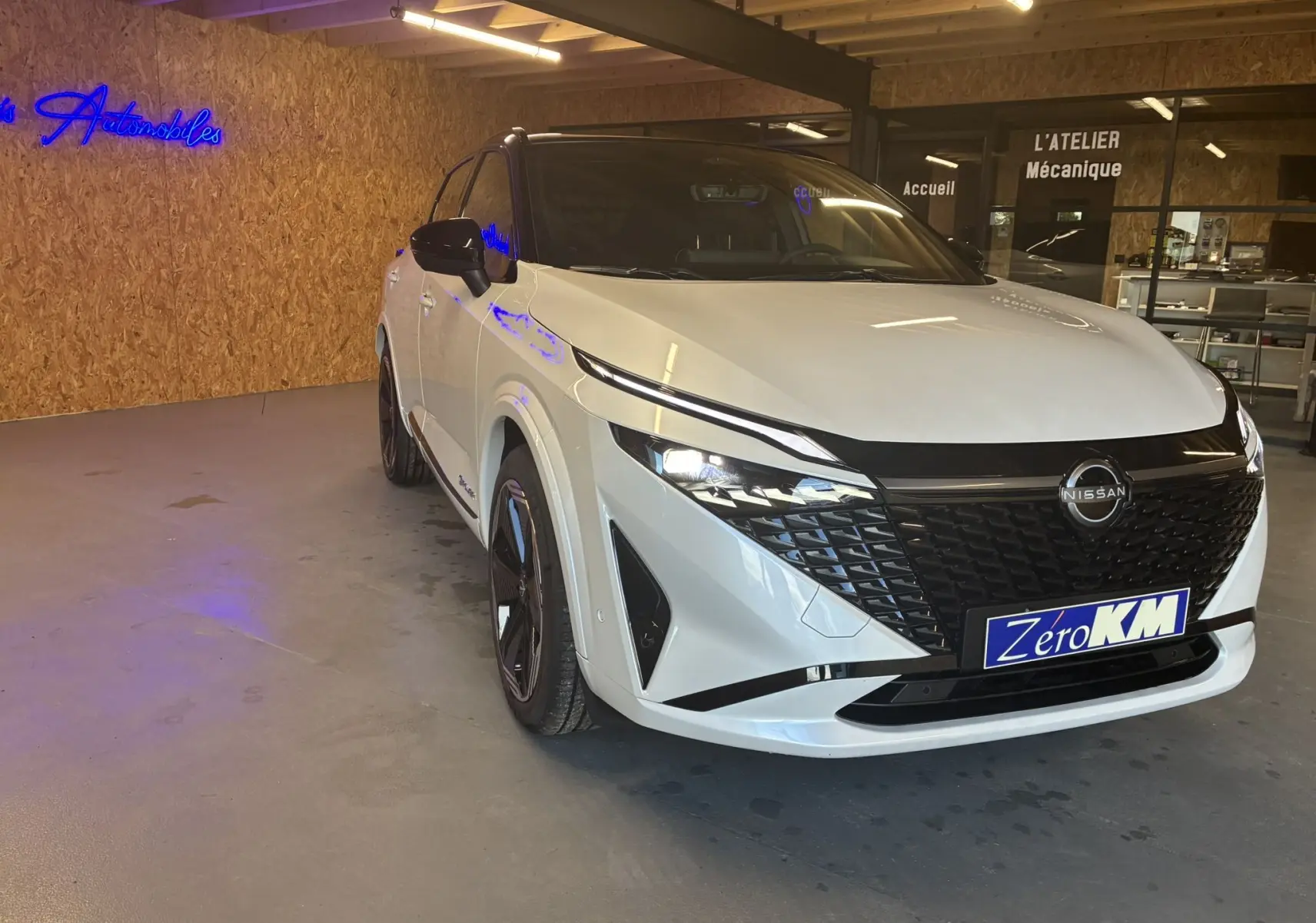 Nissan Qashqai blanc nacré avec toit noir, vue 3/4 avant droit, dans un showroom avec éclairage intérieur.