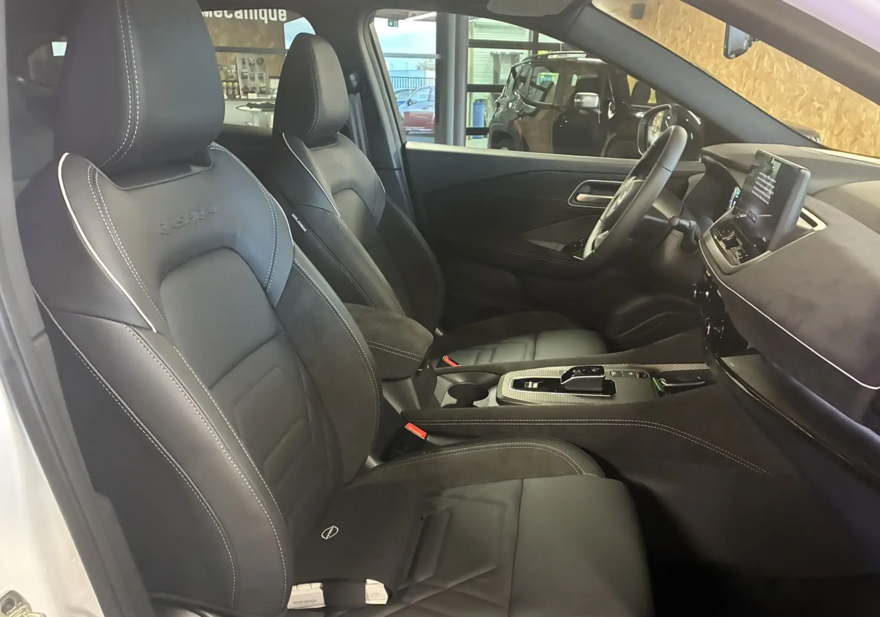 Intérieur du Nissan Qashqai 2025 vu côté conducteur, sièges noirs en cuir et alcantara avec surpiqûres blanches.