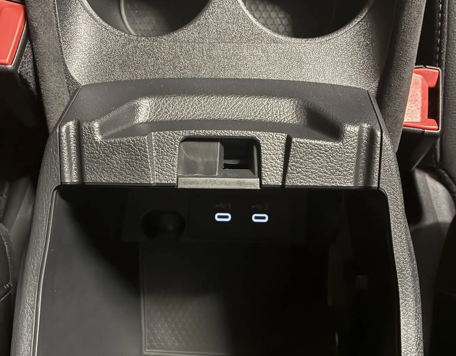 Gros plan sur la console centrale noire du Nissan Qashqai 2025, avec porte-gobelets et ports USB éclairés.