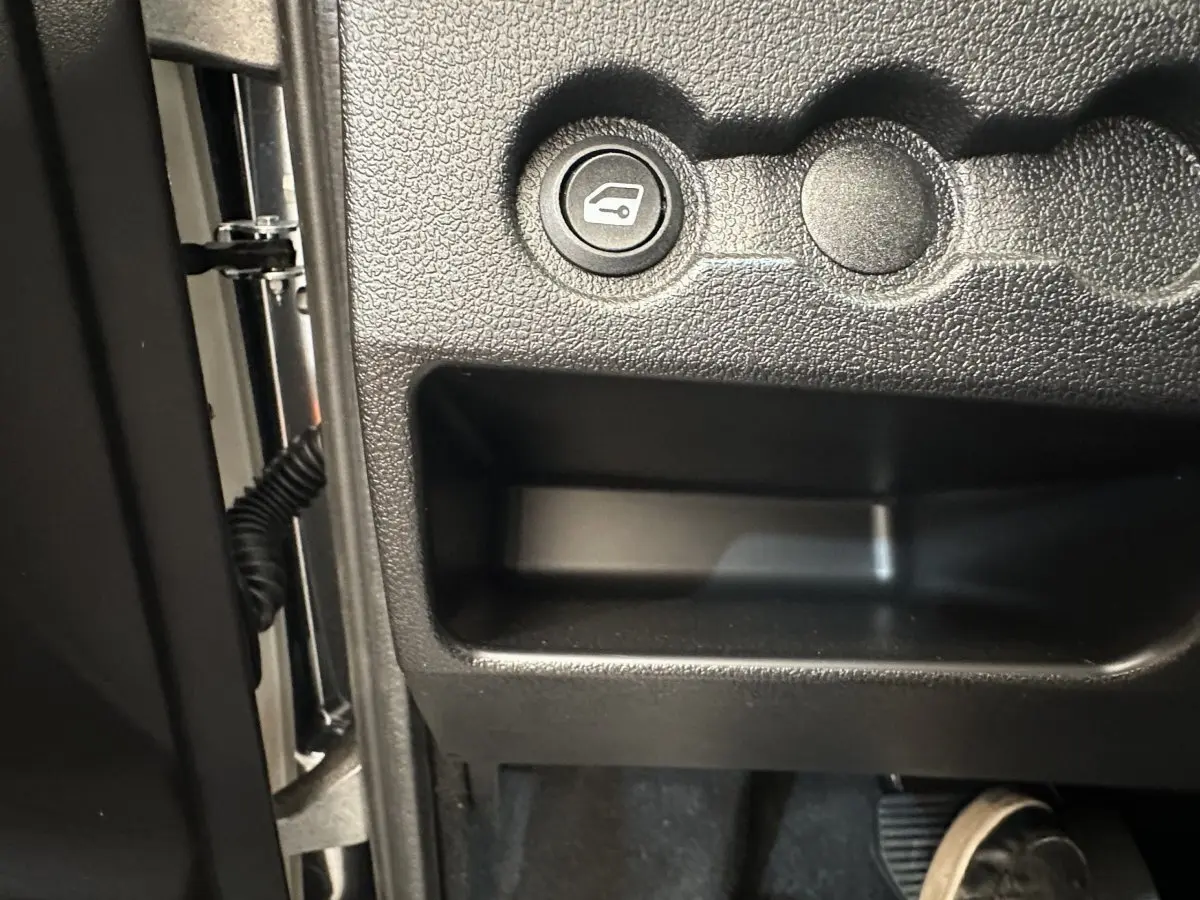 Détail du bouton d'ouverture du coffre côté conducteur dans l'habitacle noir de l'AIXAM AMBITION E CITY PACK 2025.