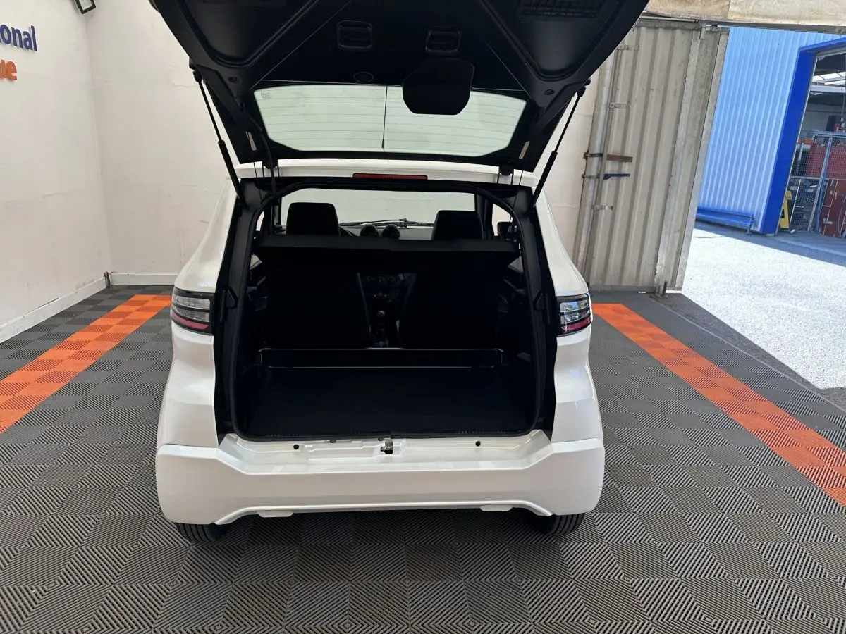 Vue arrière d'une AIXAM AMBITION E CITY PACK blanche 2025 avec coffre ouvert dans un garage éclairé.