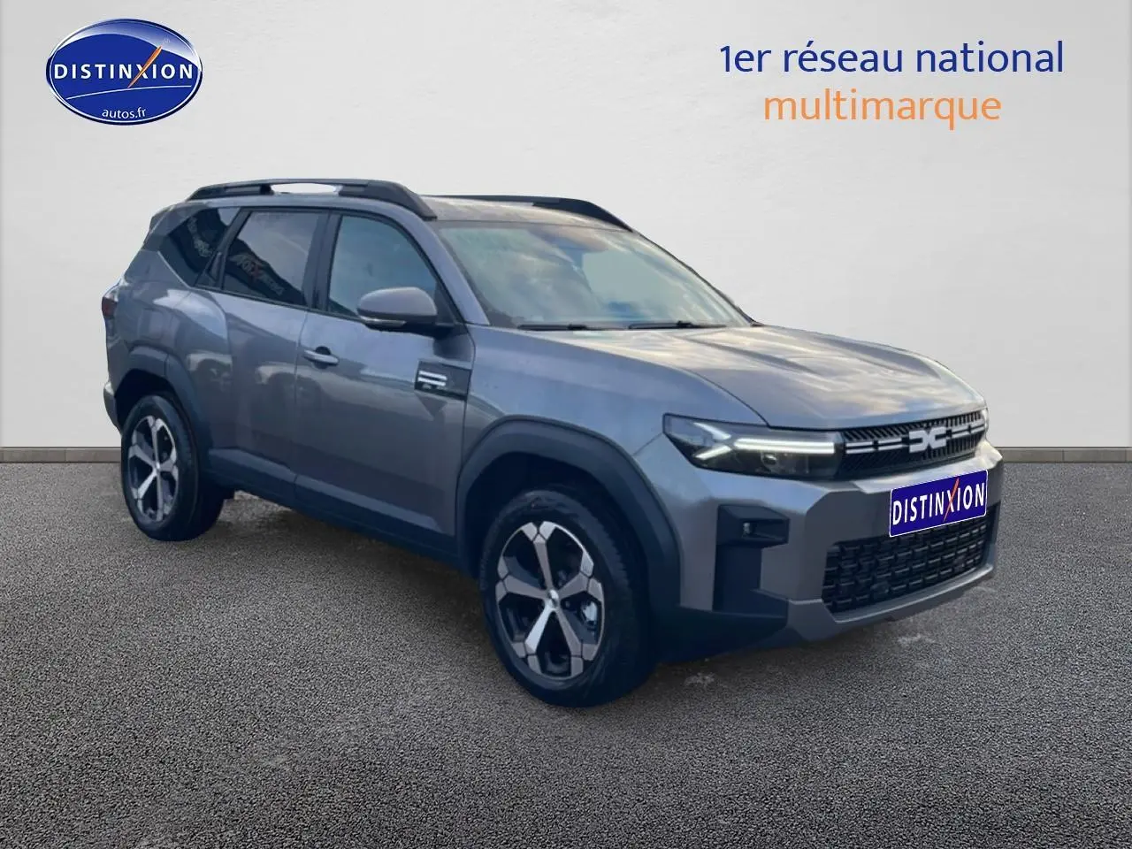 SUV Dacia Bigster gris schiste en 3/4 avant droit avec jantes alliage diamantées et barres de toit noires.