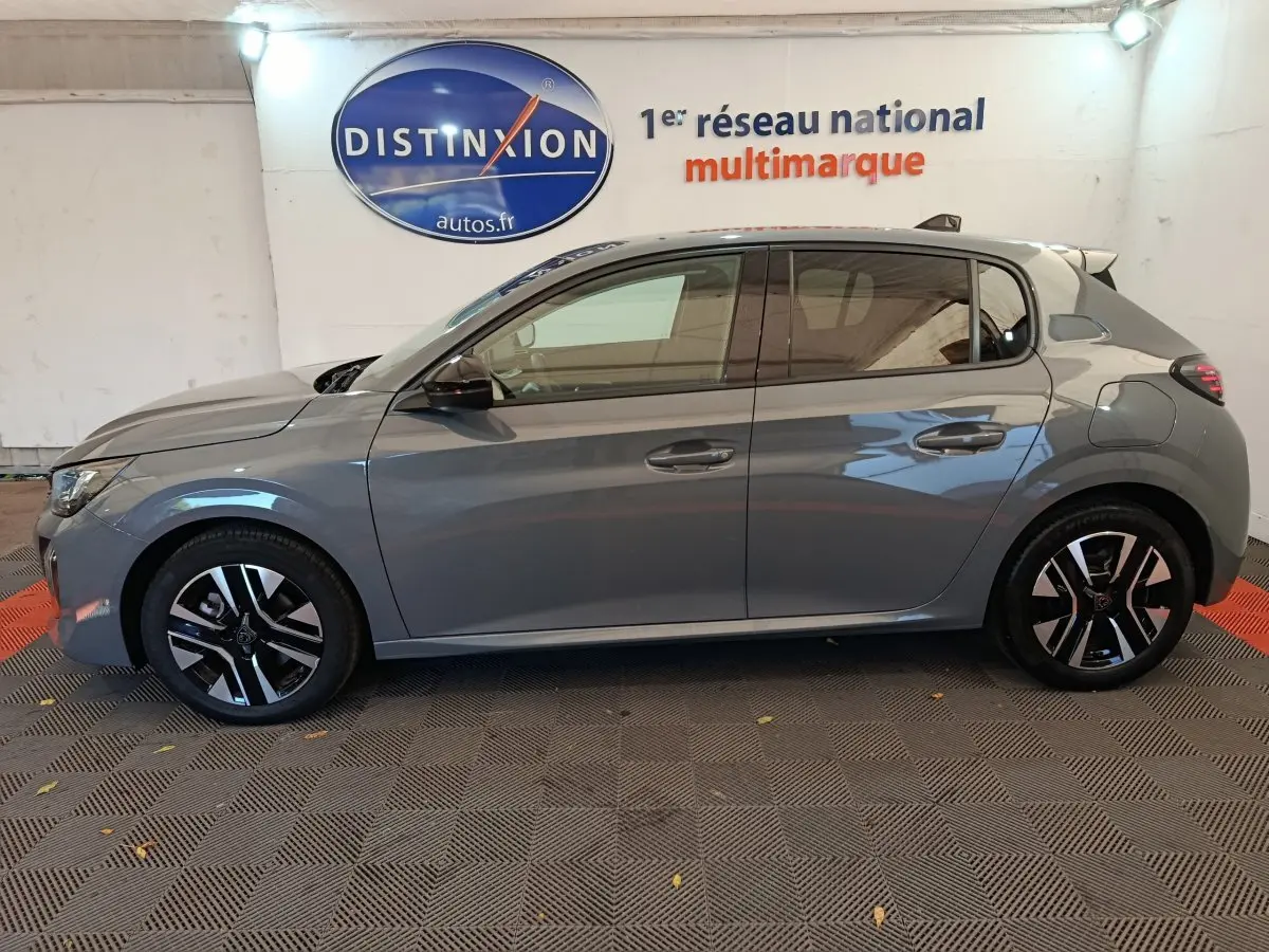 Profil côté gauche d'une Peugeot 208 gris foncé 2025, avec jantes noires et détails modernes visibles en intérieur showroom.
