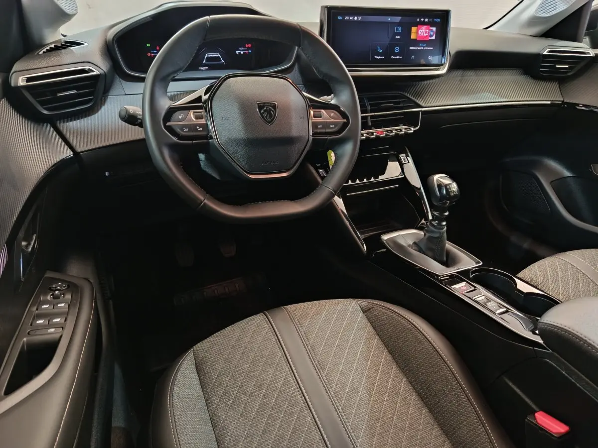 Vue intérieure centrée sur le volant et la console centrale de la Peugeot 208 gris foncé avec boîte manuelle et écran tactile.