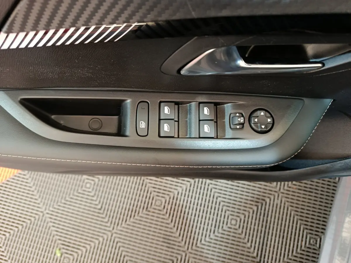 Détail des commandes des vitres et rétroviseurs sur la porte côté conducteur d'une Peugeot 208 gris foncé.