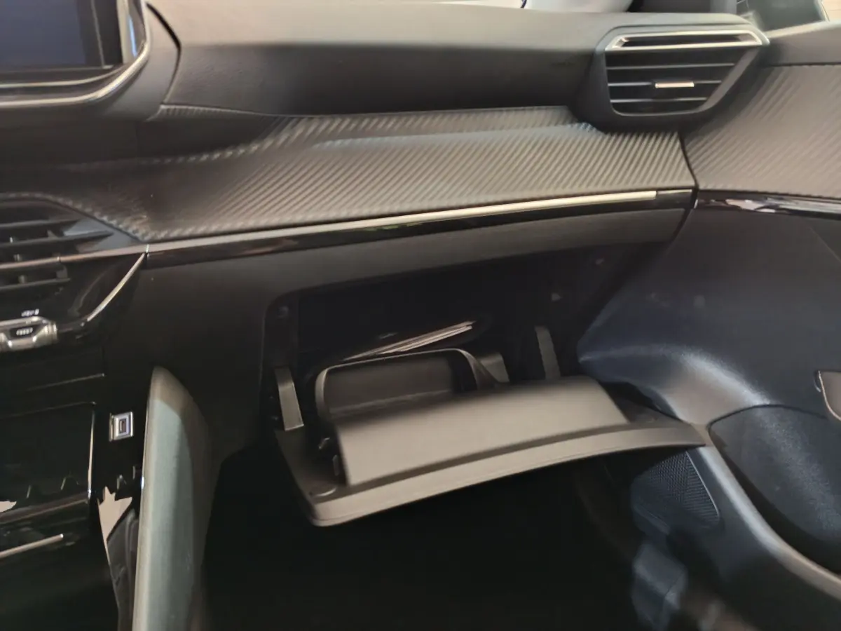 Vue intérieure du tableau de bord gris foncé de la Peugeot 208 2025 avec boîte à gants ouverte côté passager.