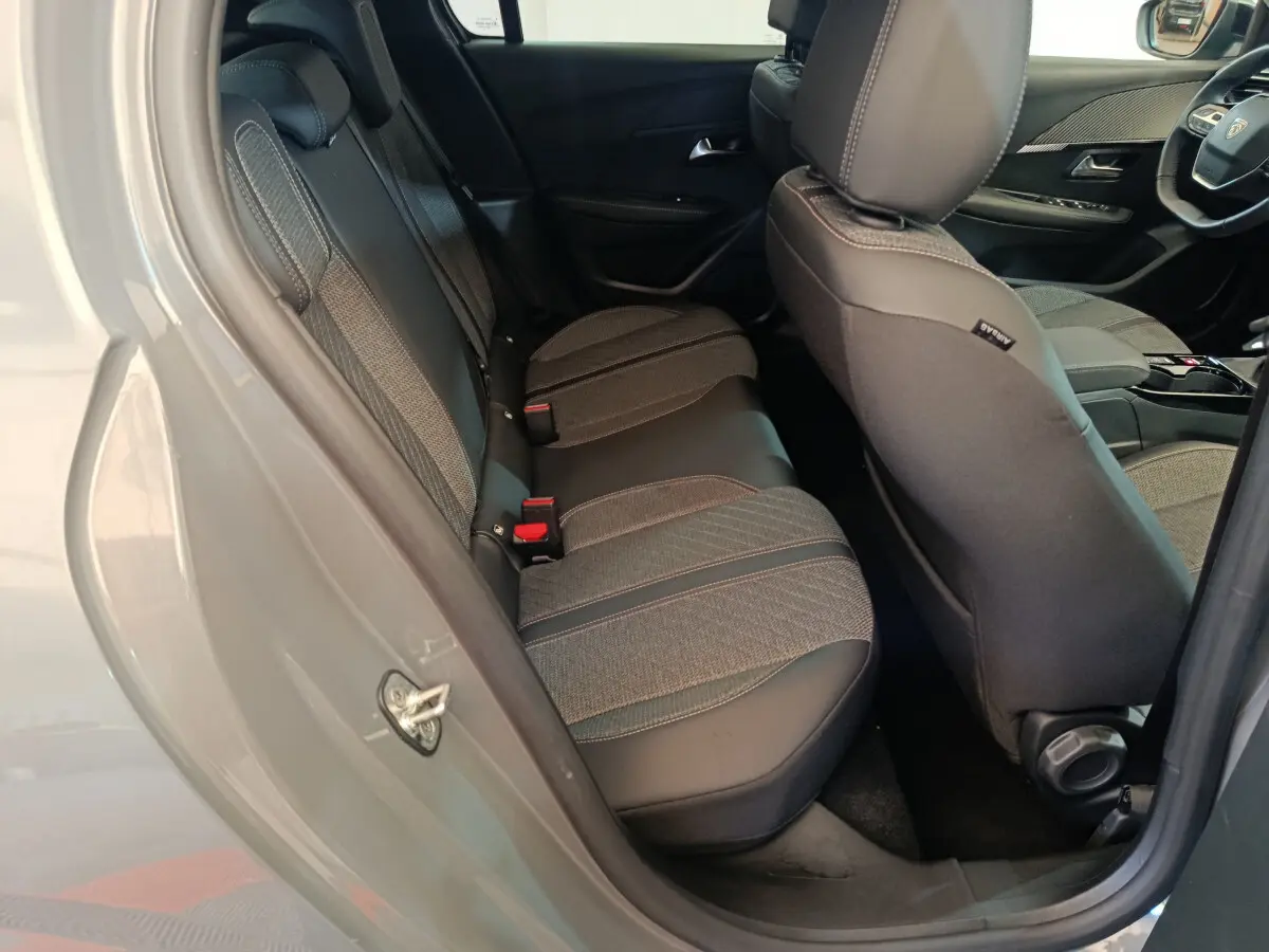 Vue intérieure côté arrière gauche de la Peugeot 208 gris foncé, montrant les sièges arrière en tissu et cuir.