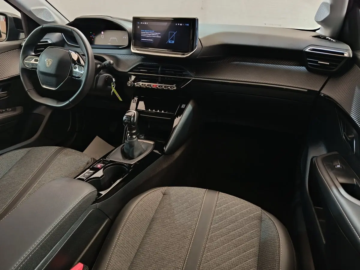 Intérieur de la Peugeot 208 PureTech 100 S&S Allure 2025, vue côté conducteur, tableau de bord gris foncé avec écran tactile.