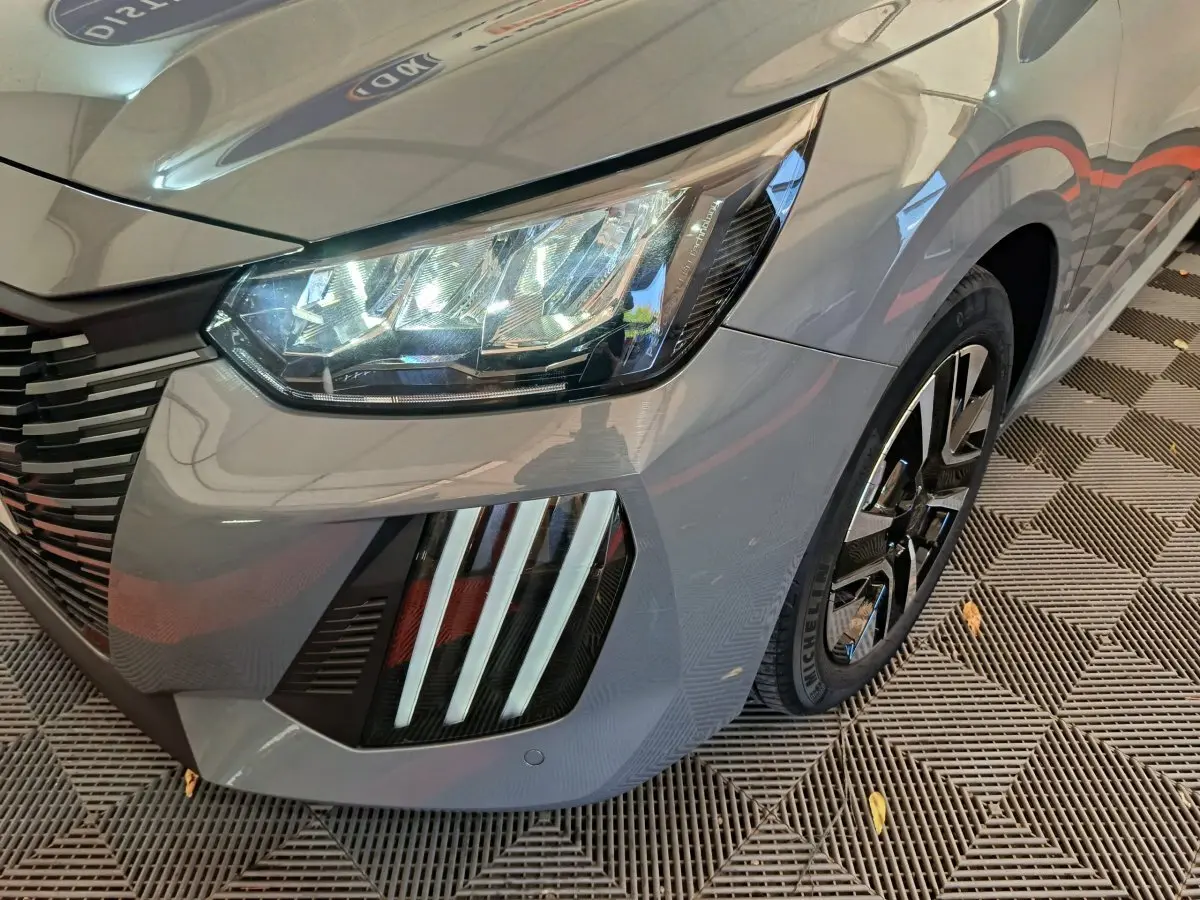 Gros plan sur l'avant droit gris foncé du Peugeot 208 2025, mettant en valeur le phare LED et la jante noire brillante.