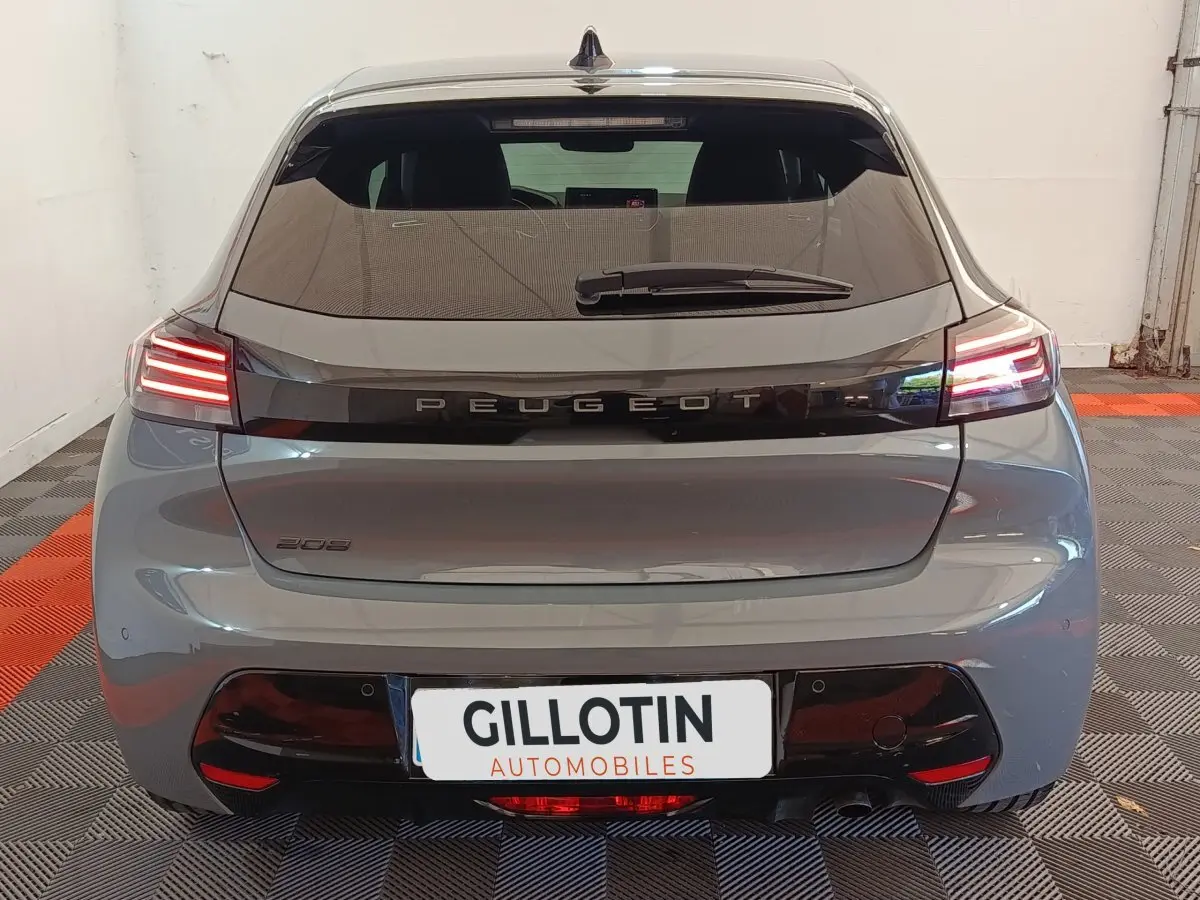 Vue arrière d'une Peugeot 208 gris foncé avec feux arrière allumés et logo Peugeot central sur le hayon.