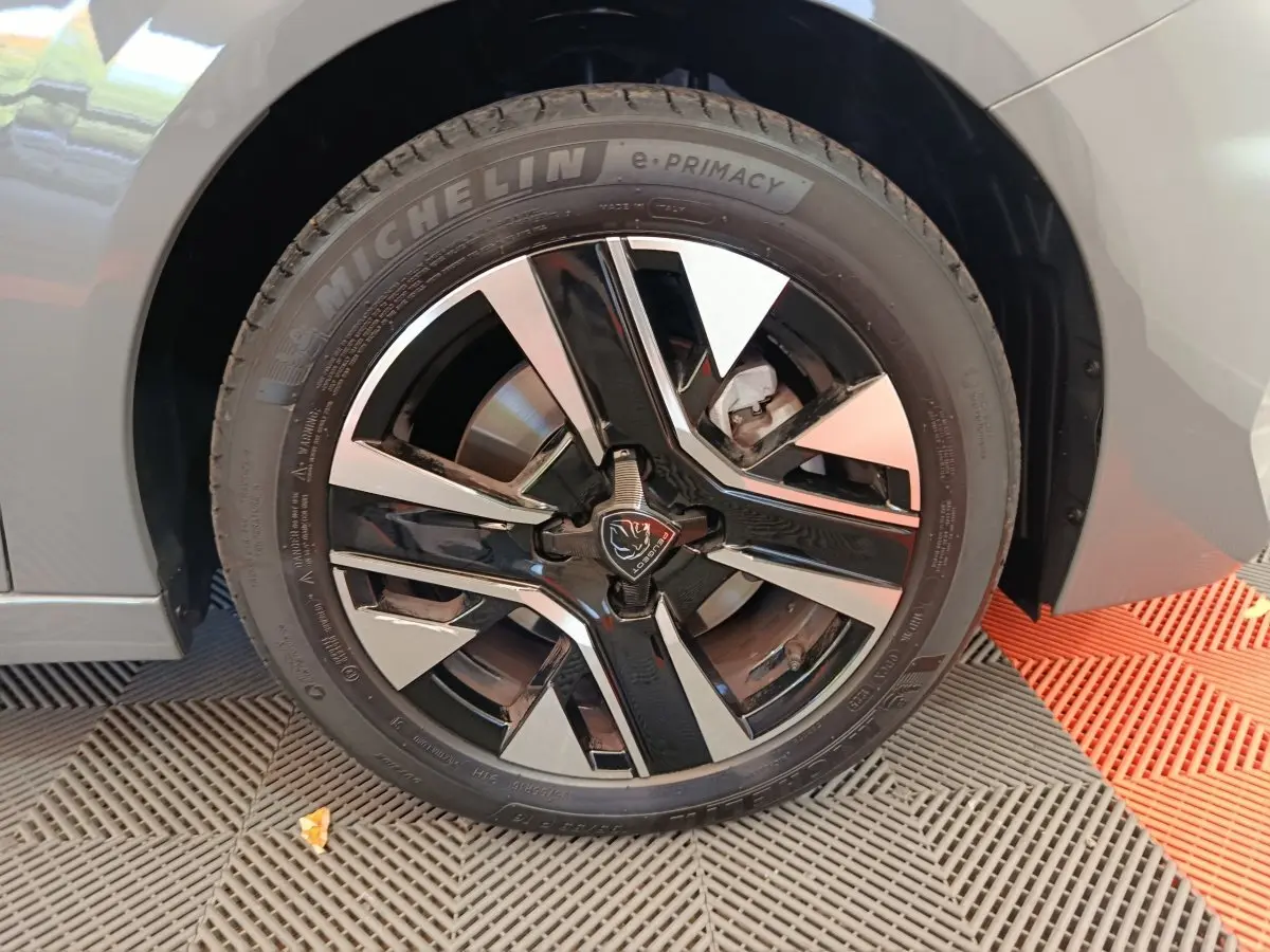 Gros plan sur la roue avant droite d’une Peugeot 208 gris foncé avec jante alliage bicolore et logo lion central.