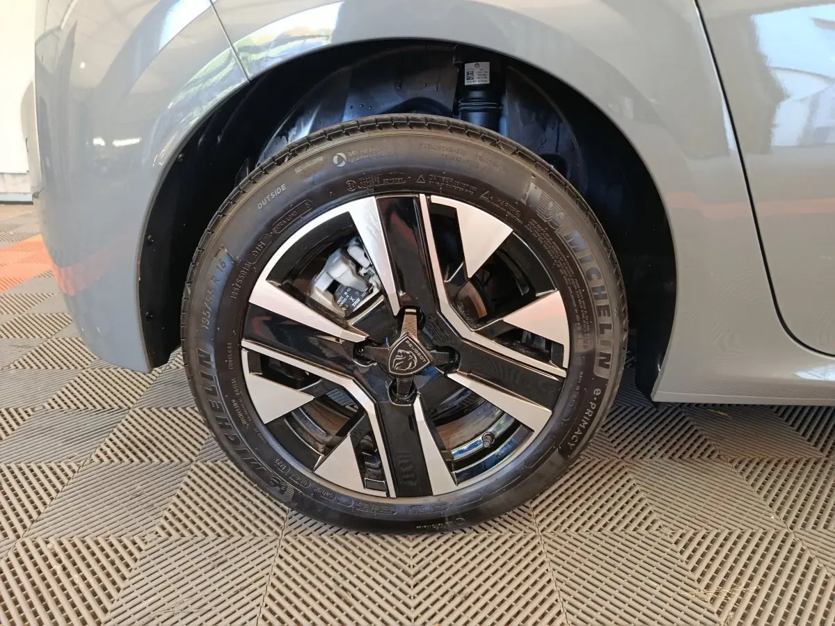 Gros plan sur la roue avant droite de la Peugeot 208 gris foncé, mettant en valeur la jante alliage bicolore au design moderne.